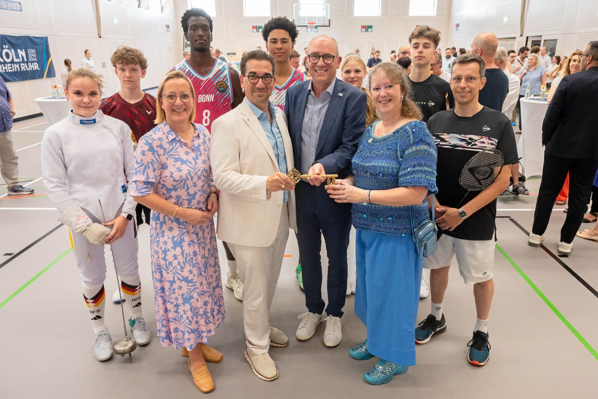 Symbolische Schlüsselübergabe zur Fertigstellung der neuen Sporthalle am Tannenbusch-Gymnasium - vordere Reihe v.l.: Bezirksbürgermeisterin Nicole Bonnie, OB Guido Déus, Schulleiter Eike Schulz und Staatssekretärin Andrea Milz. Hinten v.l.: die Schüler*innen Chiara Rott, Tom Klein, Noah Kouame, Marvin Nduche, Eva Heiden, Jari Hannes sowie Badminton-Trainer Marc Hannes.