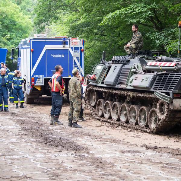 Das Bild zeigt Soldaten im Gespräch mit Mitarbeitenden des THW. Der Soldat sitzt an der Steinbachtalsperre auf einem Panzer.