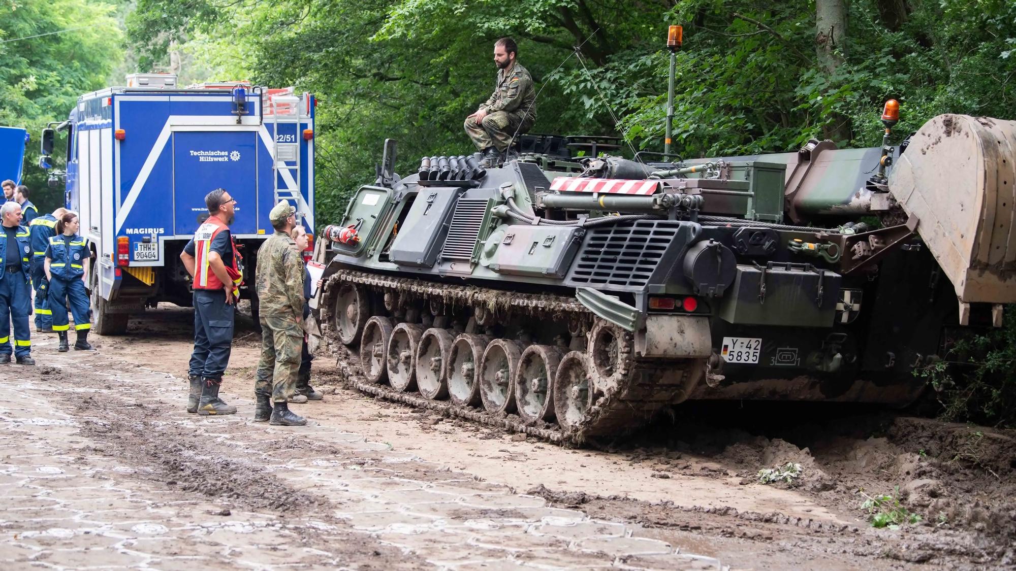 Das Bild zeigt Soldaten im Gespräch mit Mitarbeitenden des THW. Der Soldat sitzt an der Steinbachtalsperre auf einem Panzer.