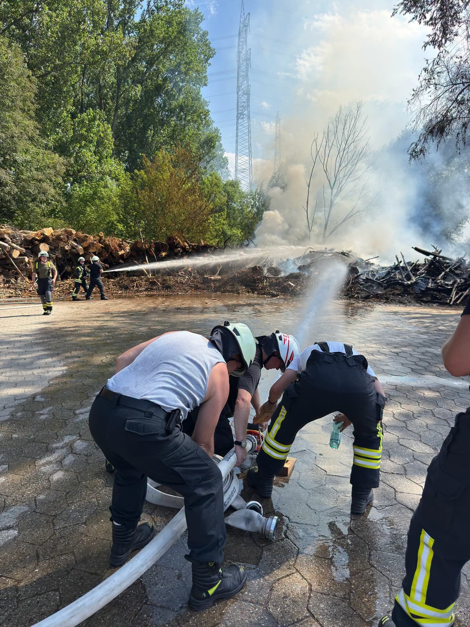 Einsatzkräfte der Feuerwehr löschen den Brand von aufgestapeltem Holz.