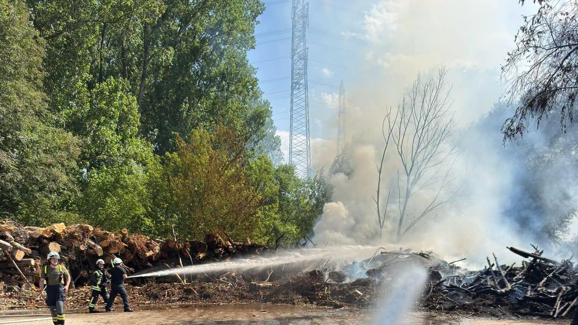 Einsatzkräfte der Feuerwehr löschen den Brand von aufgestapeltem Holz.