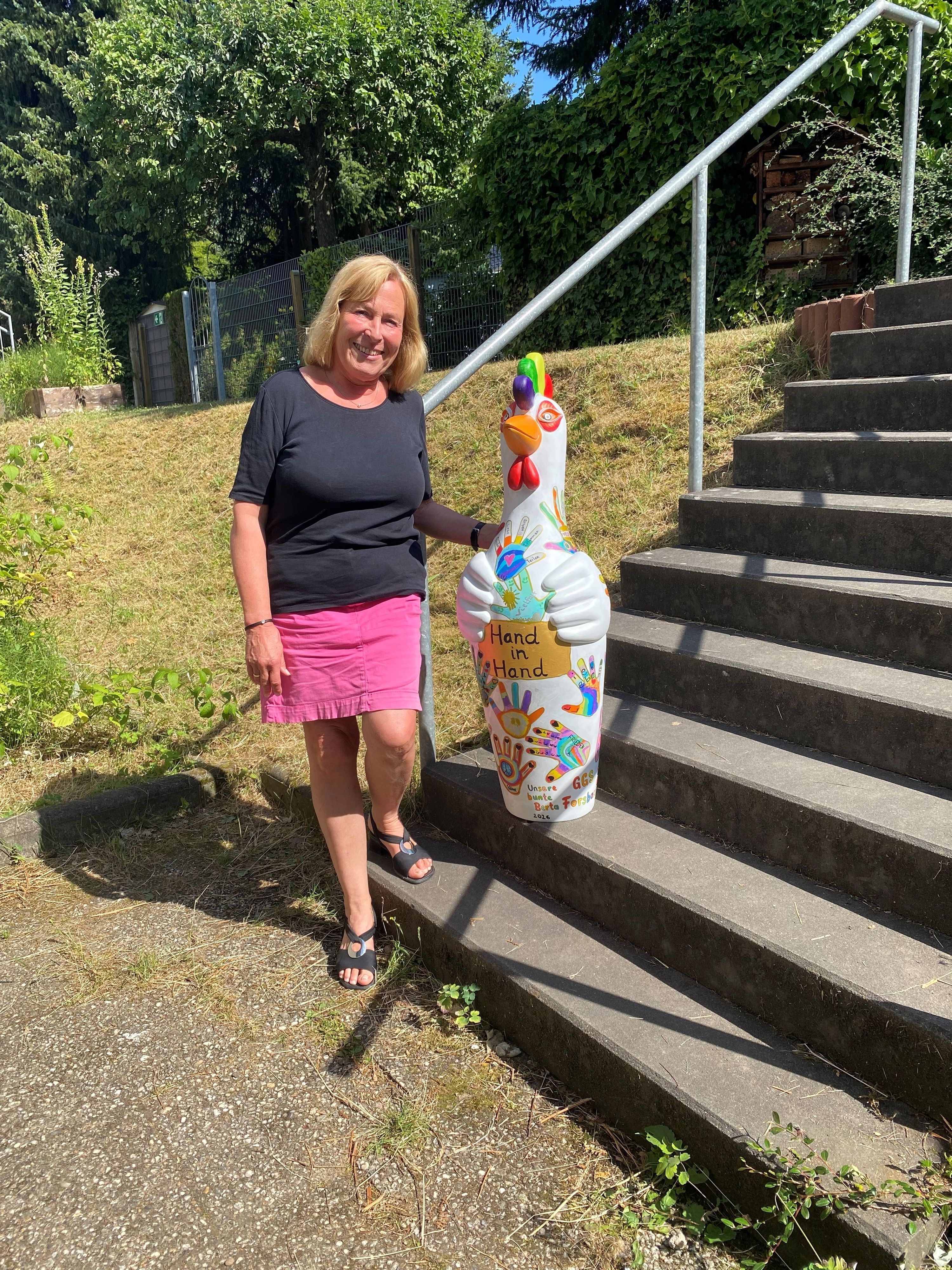Eine Frau steht neben einer bunt bemalten Skulptur, einem Huhn