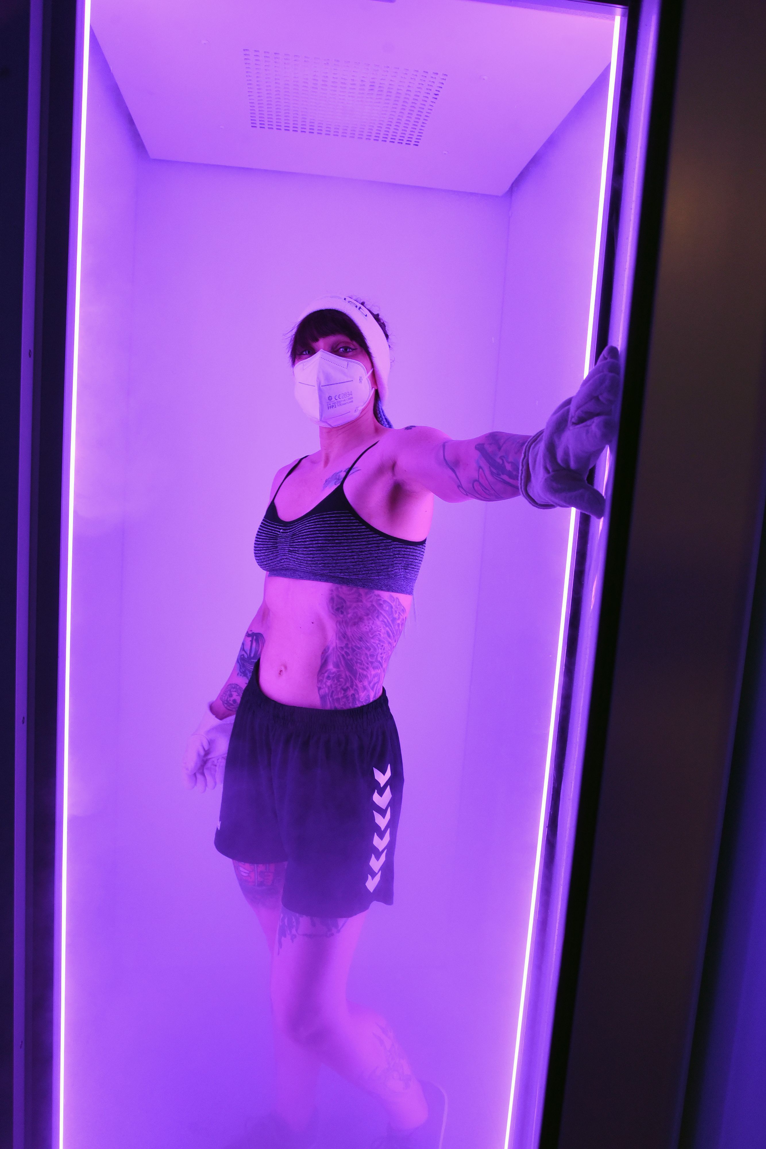 Eine Frau geht in eine Kältesauna, die lila beleuchtet ist.