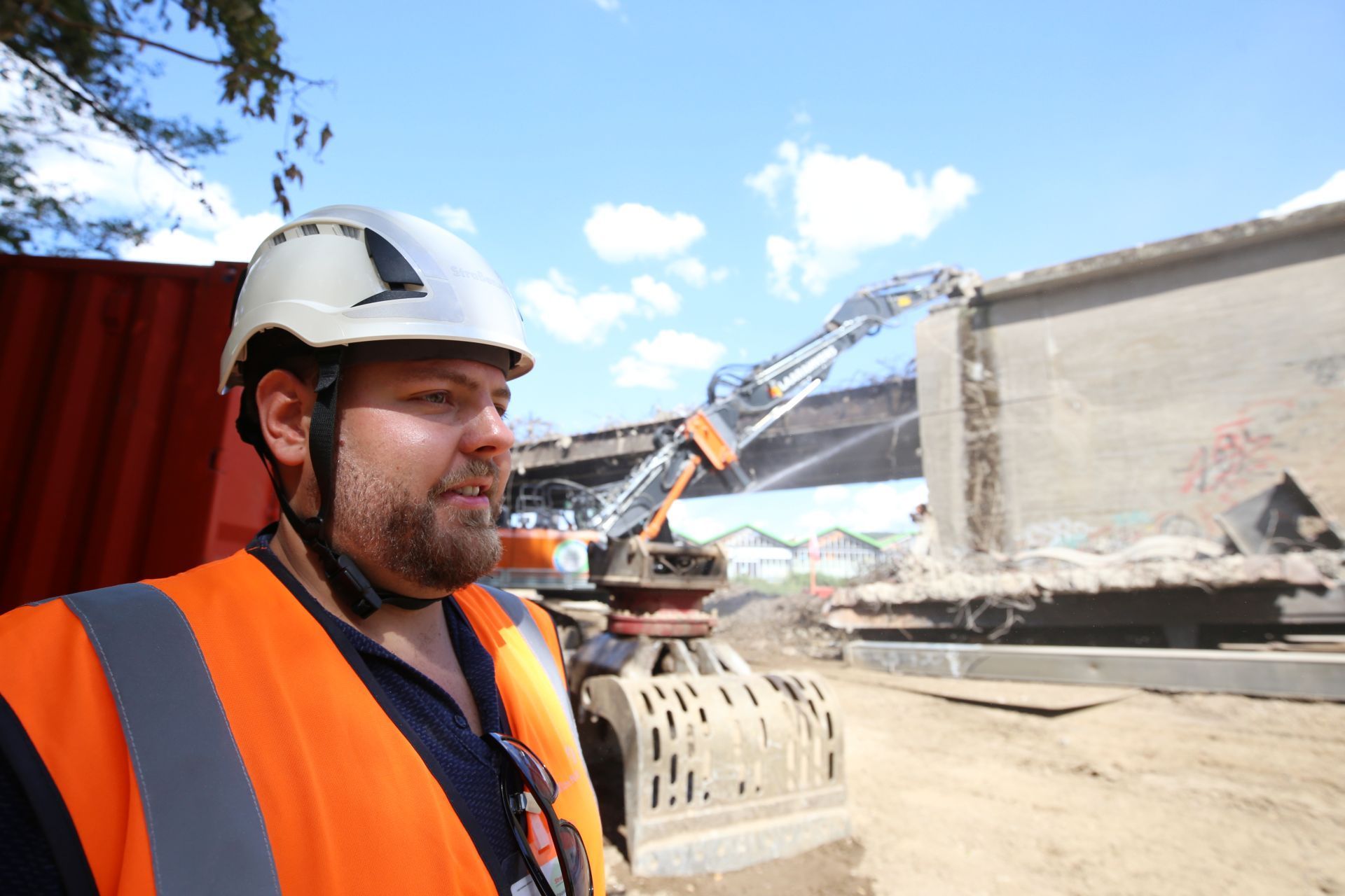 Ein Mann mit Bart und weißem Bauhelm auf einer Baustelle.