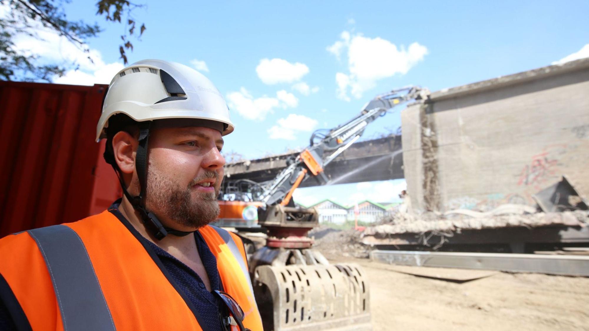 Ein Mann mit Bart und weißem Bauhelm auf einer Baustelle.
