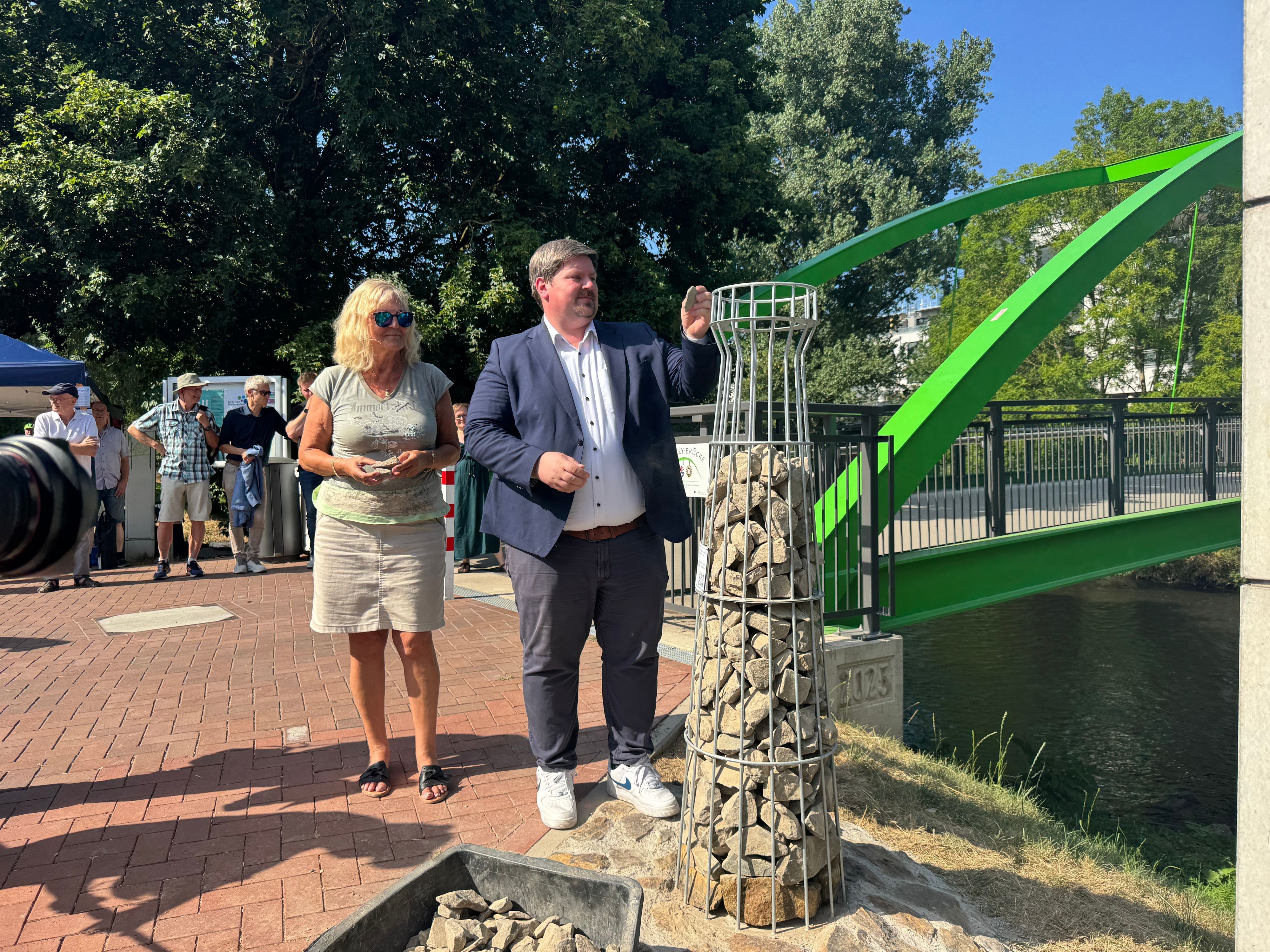 Bürgermeister Winter und Elke Plage vom Verein Wupperbogen fügen dem neuen Erinnerungsleuchtturm die letzten Steine hinzu. Die Färbung an den unteren Steinen markiert den Wasserstand nach dem Starkregen 2021.