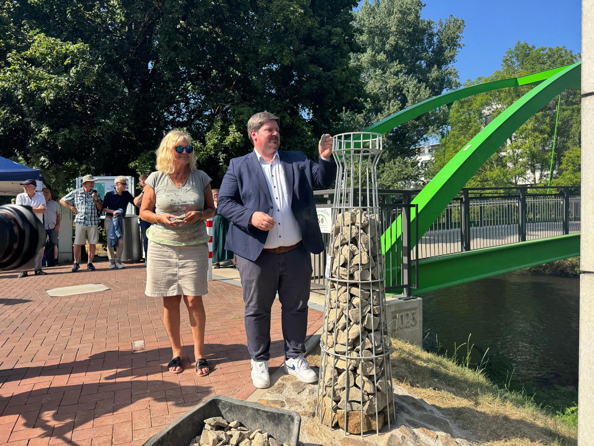 Bürgermeister Winter und Elke Plage vom Verein Wupperbogen fügen dem neuen Erinnerungsleuchtturm die letzten Steine hinzu. Die Färbung an den unteren Steinen markiert den Wasserstand nach dem Starkregen 2021.