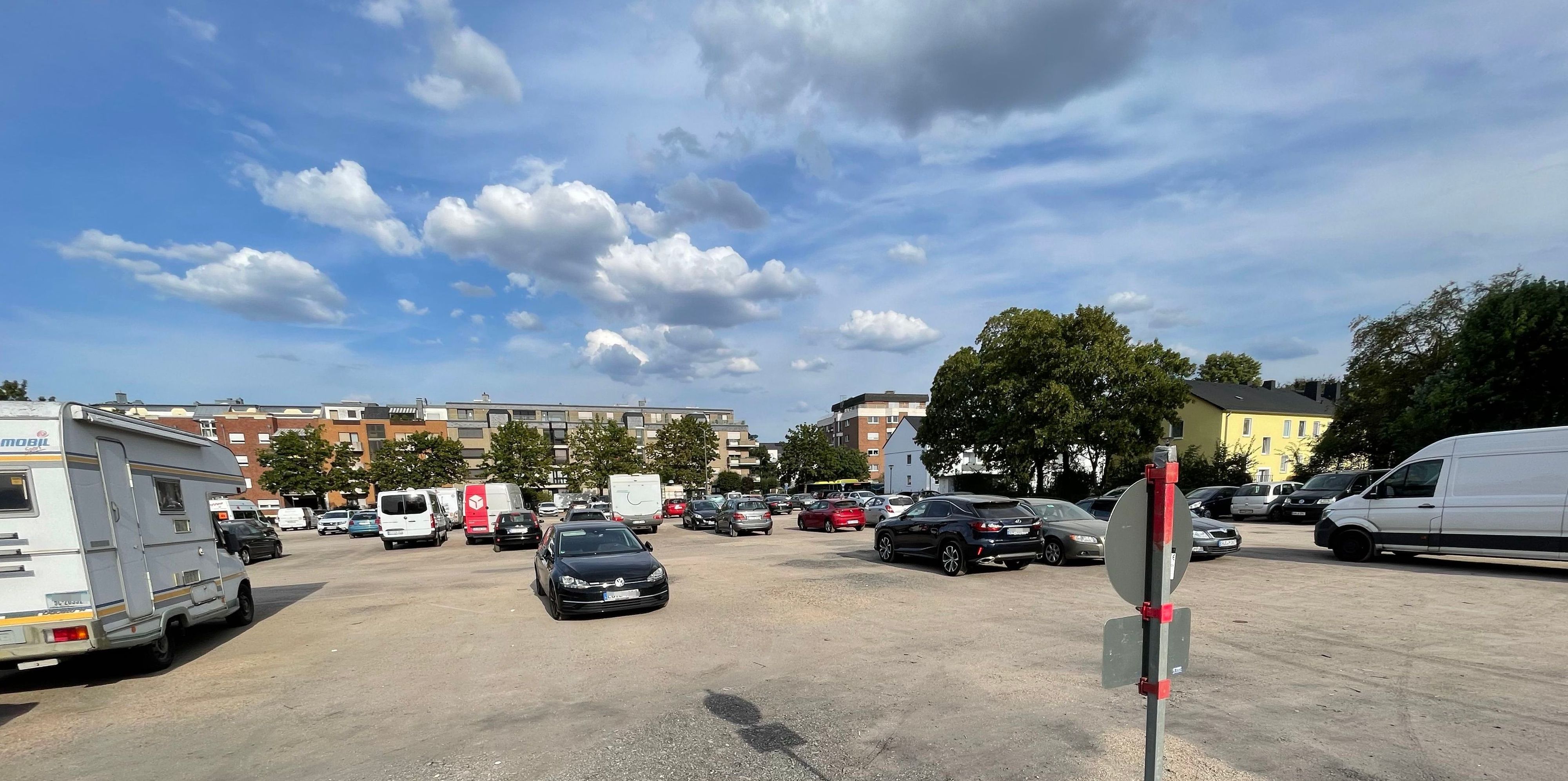 Auf dem Platz stehen Autos, Wohnmobile und Transporter. Am Rand sind Bäume platziert.