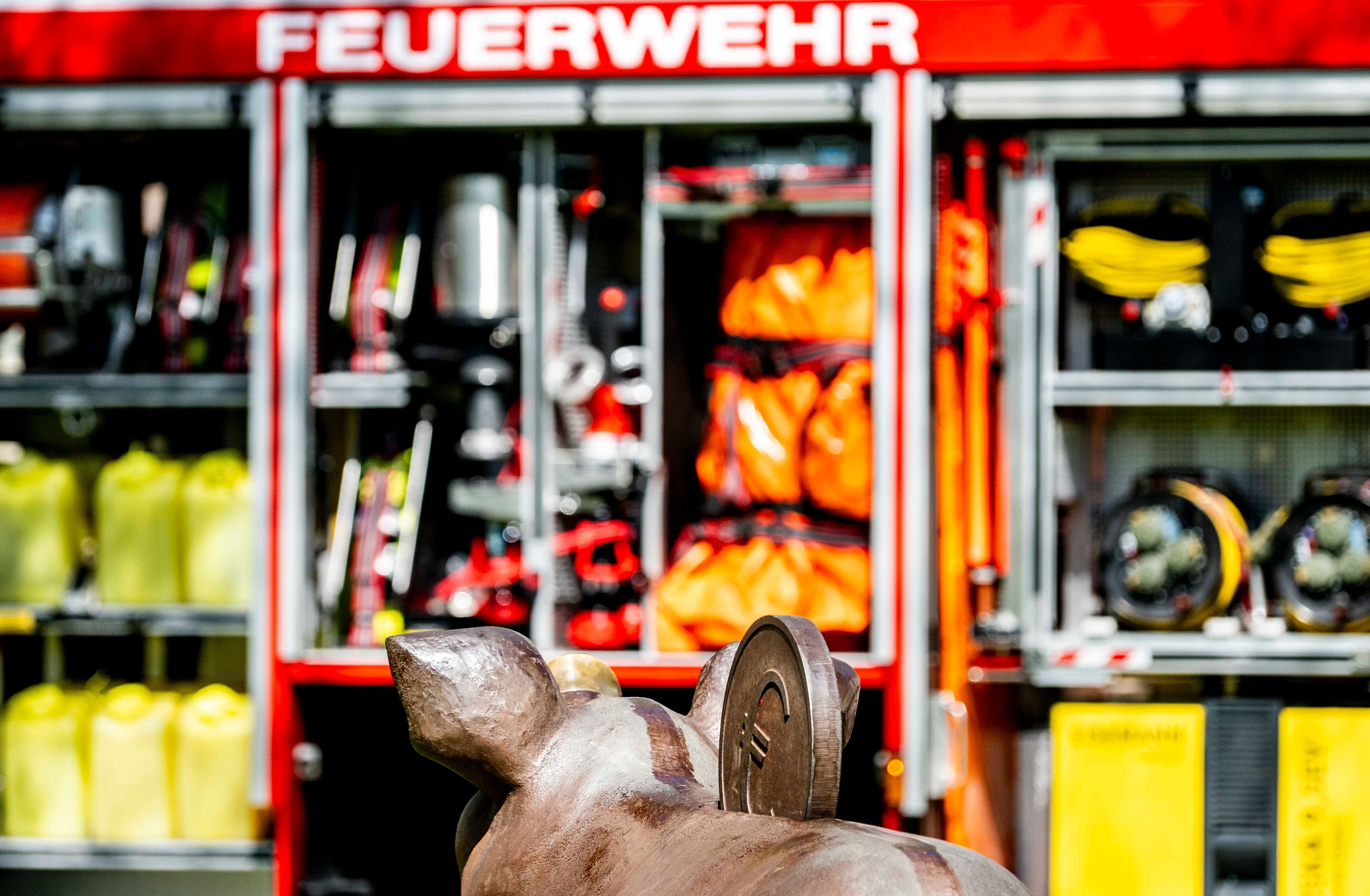 Das Bild zeigt ein Sparschwein vor einem Feuerwehrfahrzeug.