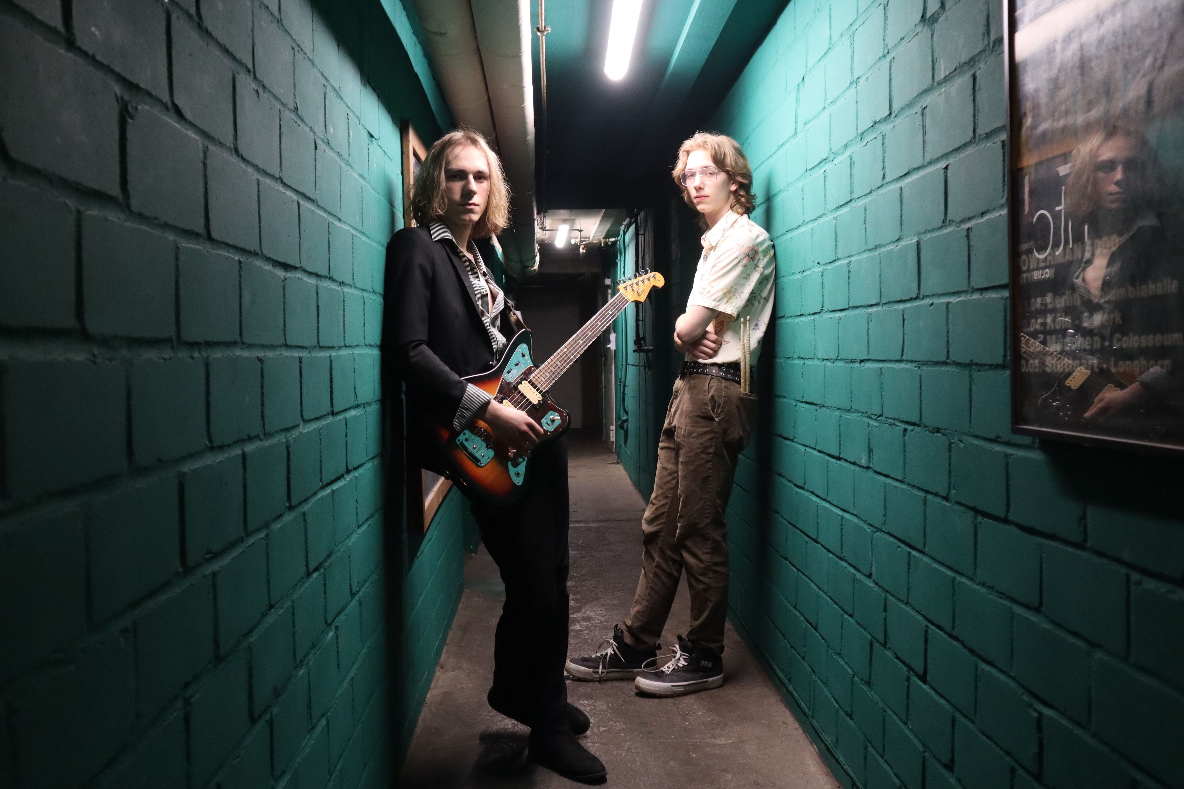 Das Foto zeigt zwei Männer in einer Gasse, einer trägt eine Gitarre.