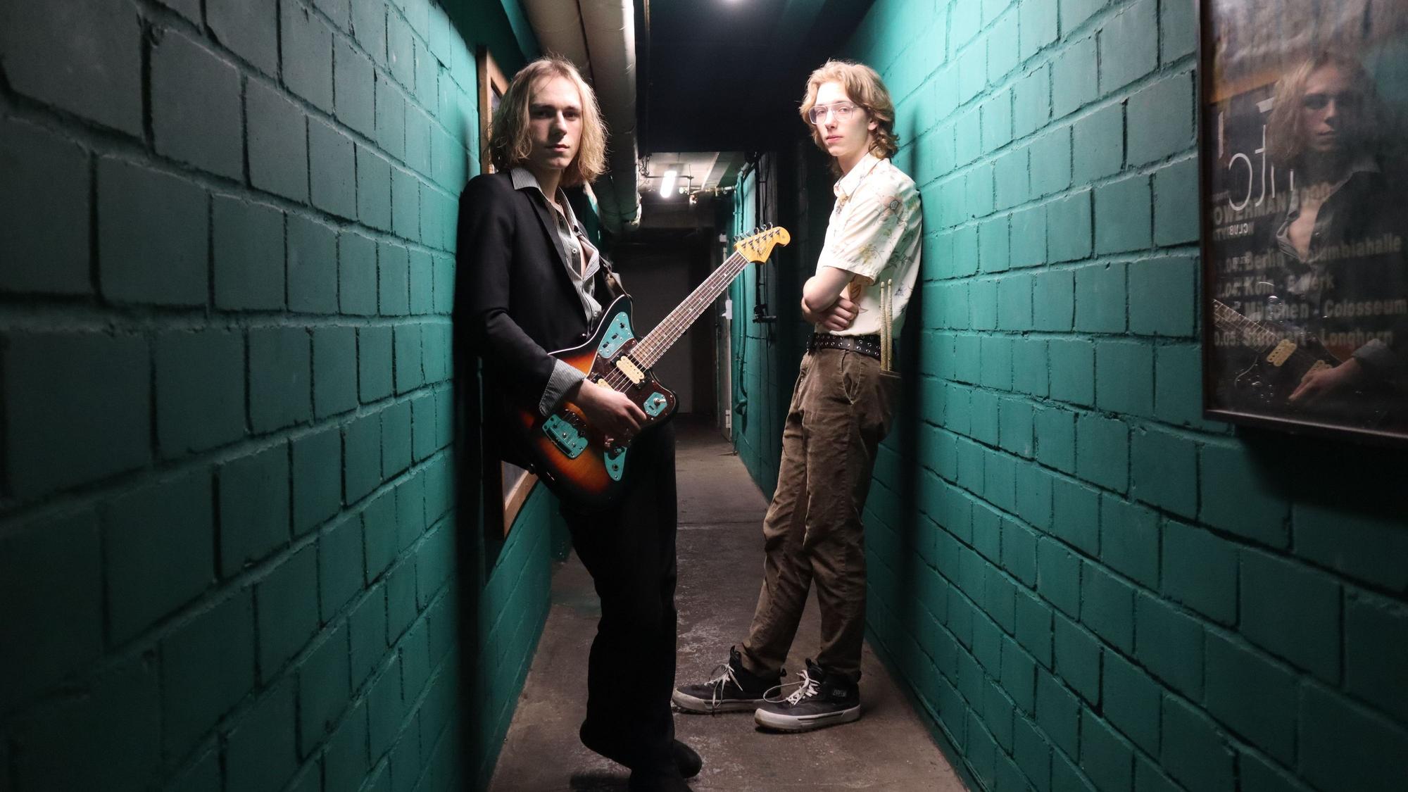 Das Foto zeigt zwei Männer in einer Gasse, einer trägt eine Gitarre.