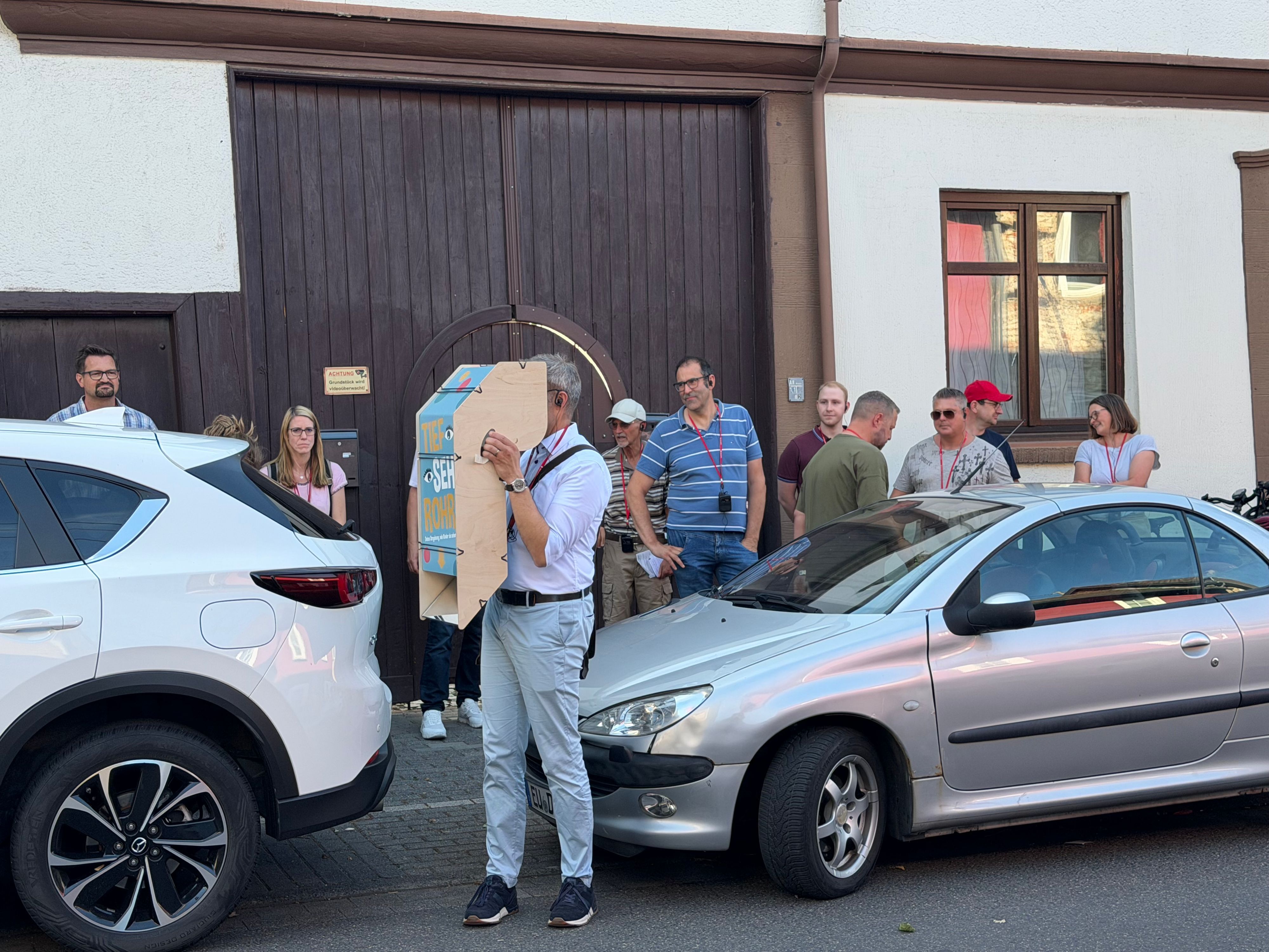 Ein Teilnehmer, der zwischen zwei geparkten Autos steht, hält sich den Apparat vor die Augen.