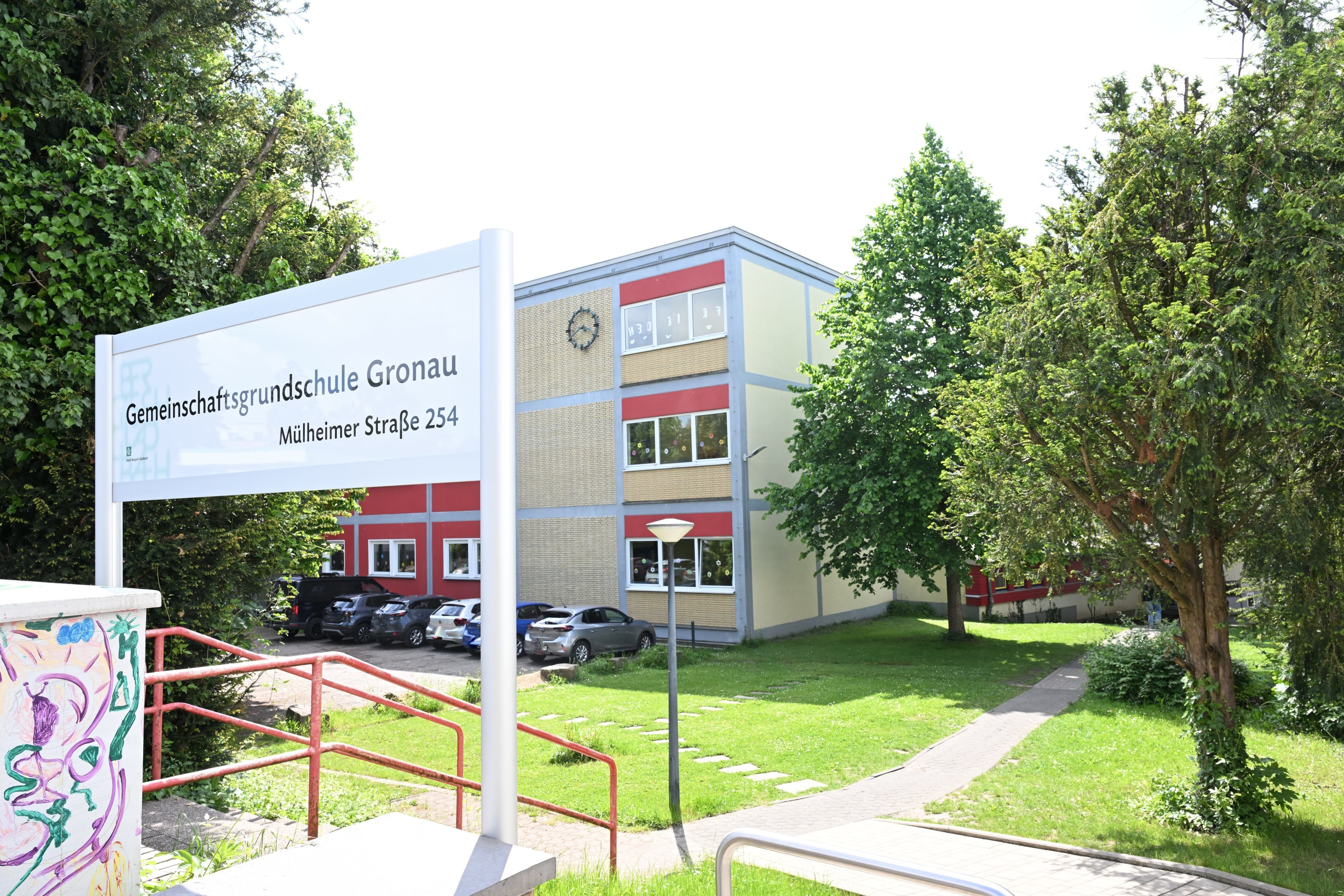 Gemeinschaftsgrundschule Gronau steht auf einem Schild im Vordergrund. Im Hintergrund ein Flachdach-Schulgebäude