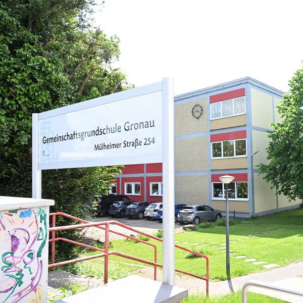Gemeinschaftsgrundschule Gronau steht auf einem Schild im Vordergrund. Im Hintergrund ein Flachdach-Schulgebäude