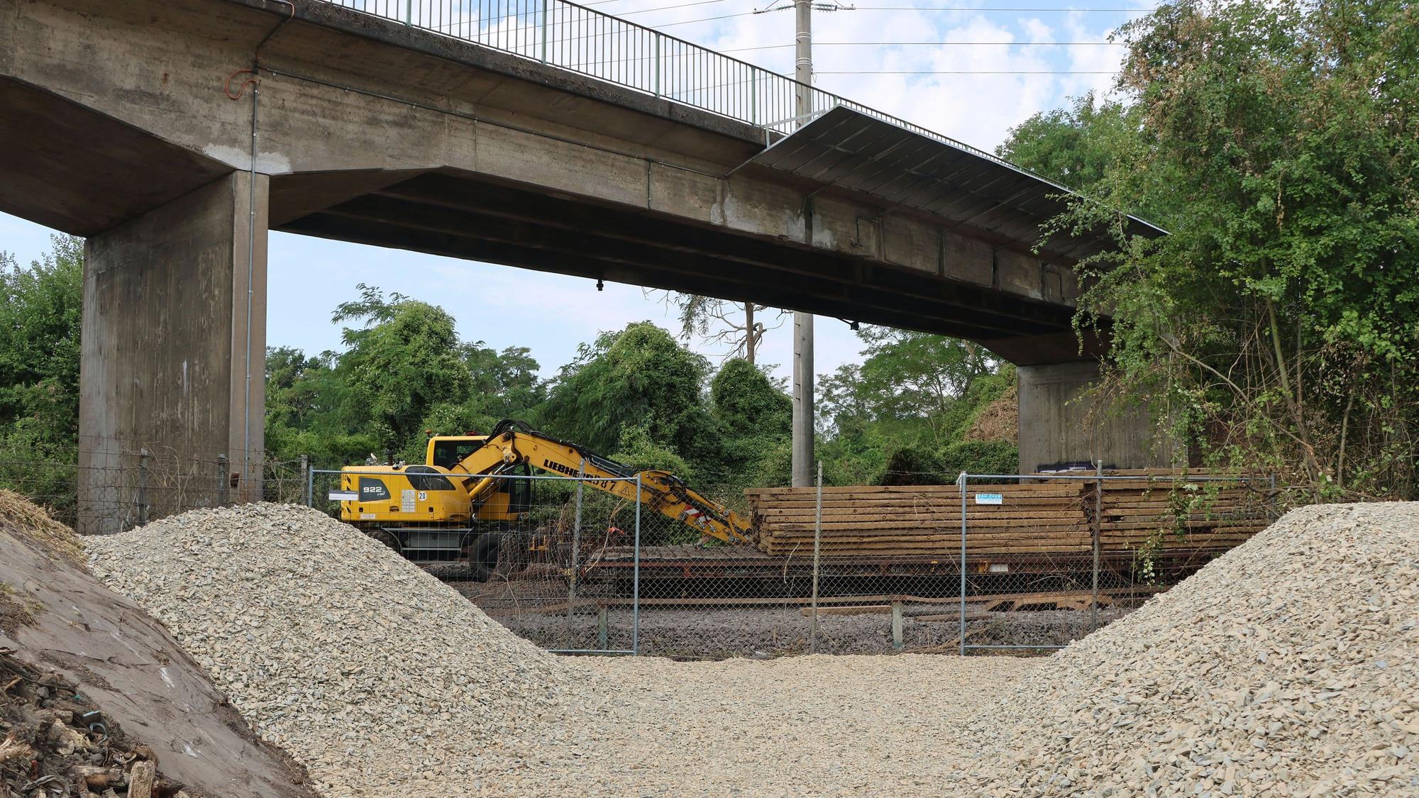Auf dem Foto sind eine Brücke, ein Bagger, Bauzäune und Schotterhaufen zu sehen.