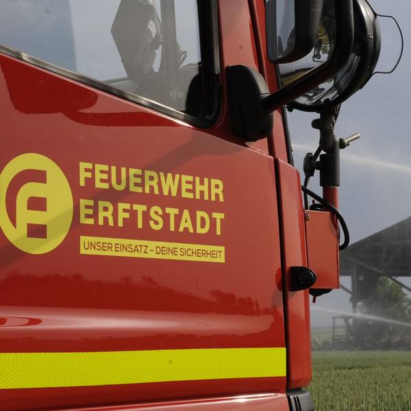 Ein Einsatzfahrzeug der Feuerwehr Erftstadt steht an einem Feld, dahinter sind eine Scheune und Löscharbeiten zu sehen.