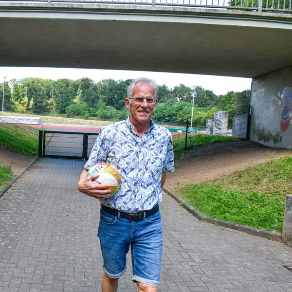 Auf dem Foto ist ein Mann vor einem Stadion zu sehen, er hat einen Fußball in der Hand.