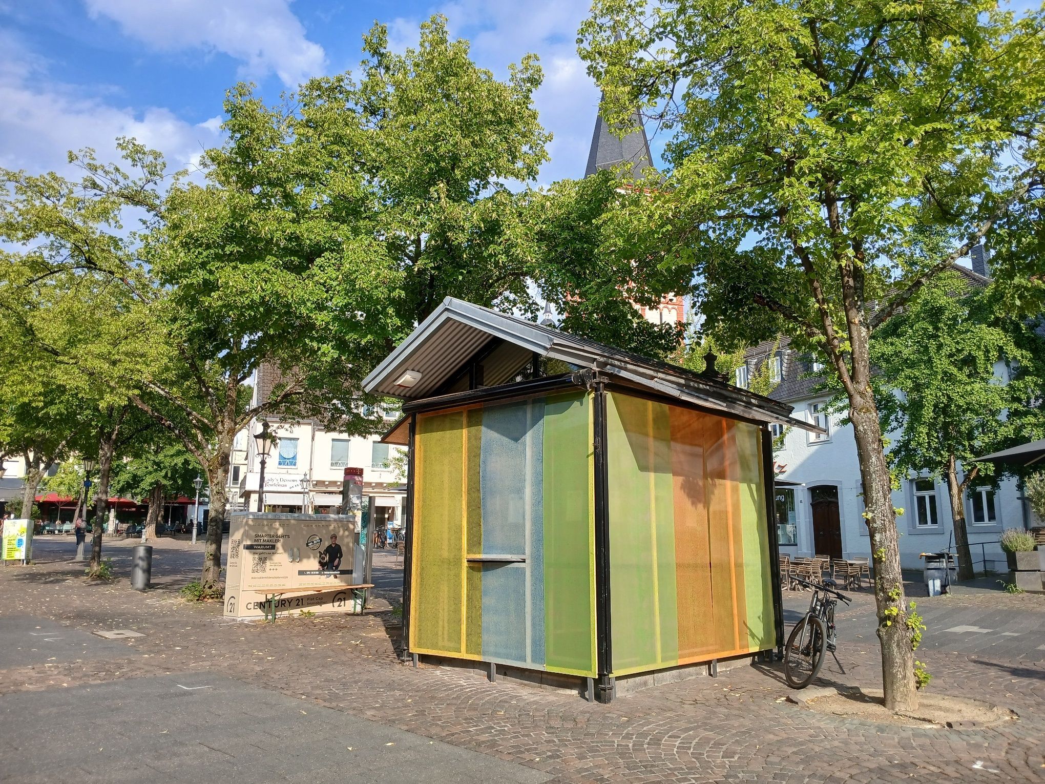 Uta Rings hat eine Fensterinstallation für den Kulturkiosk auf dem Siegburger Markt geschaffen, die sich als farbiges Band um den Pavillion zieht.