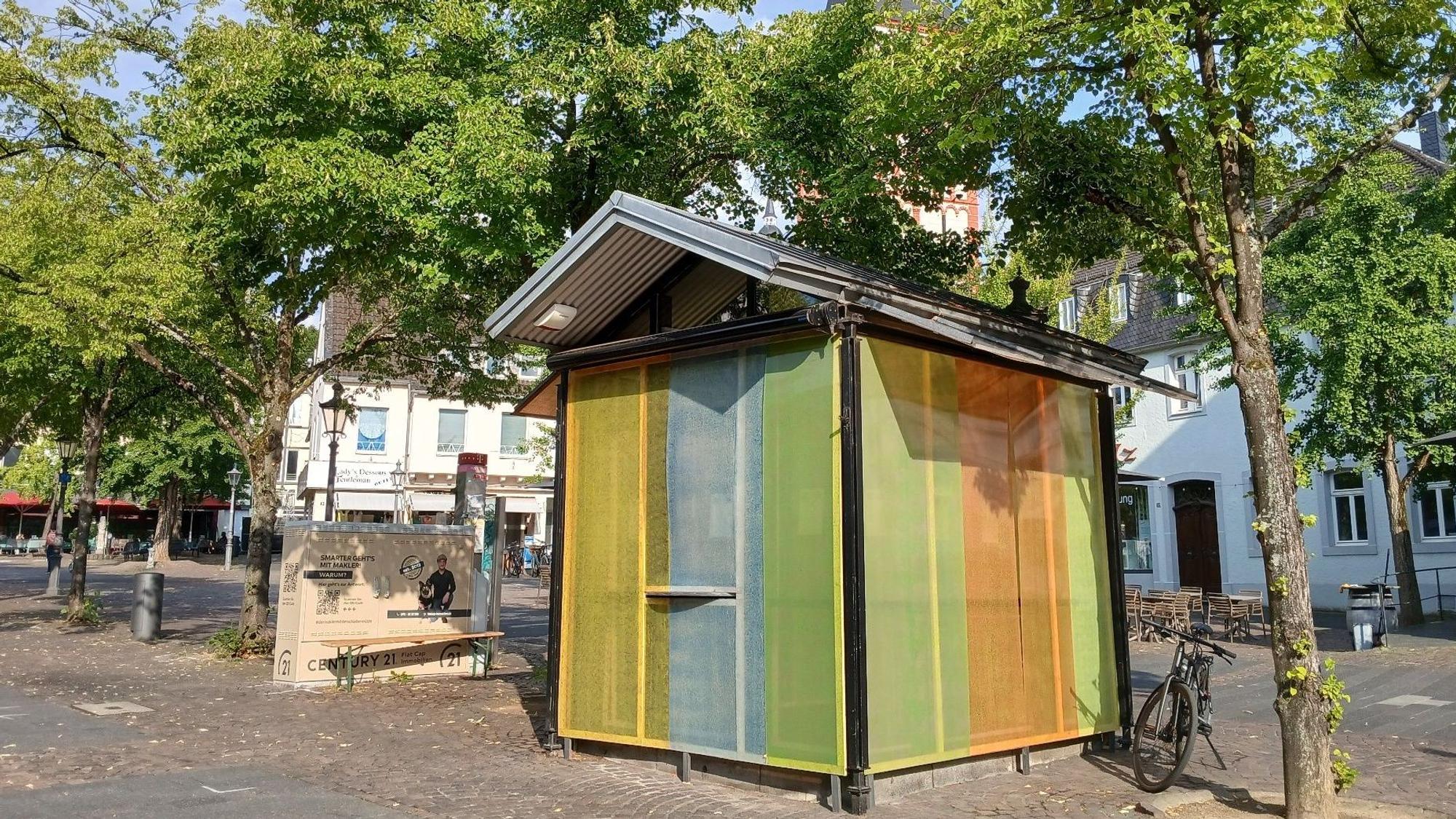 Uta Rings hat eine Fensterinstallation für den Kulturkiosk auf dem Siegburger Markt geschaffen, die sich als farbiges Band um den Pavillion zieht.