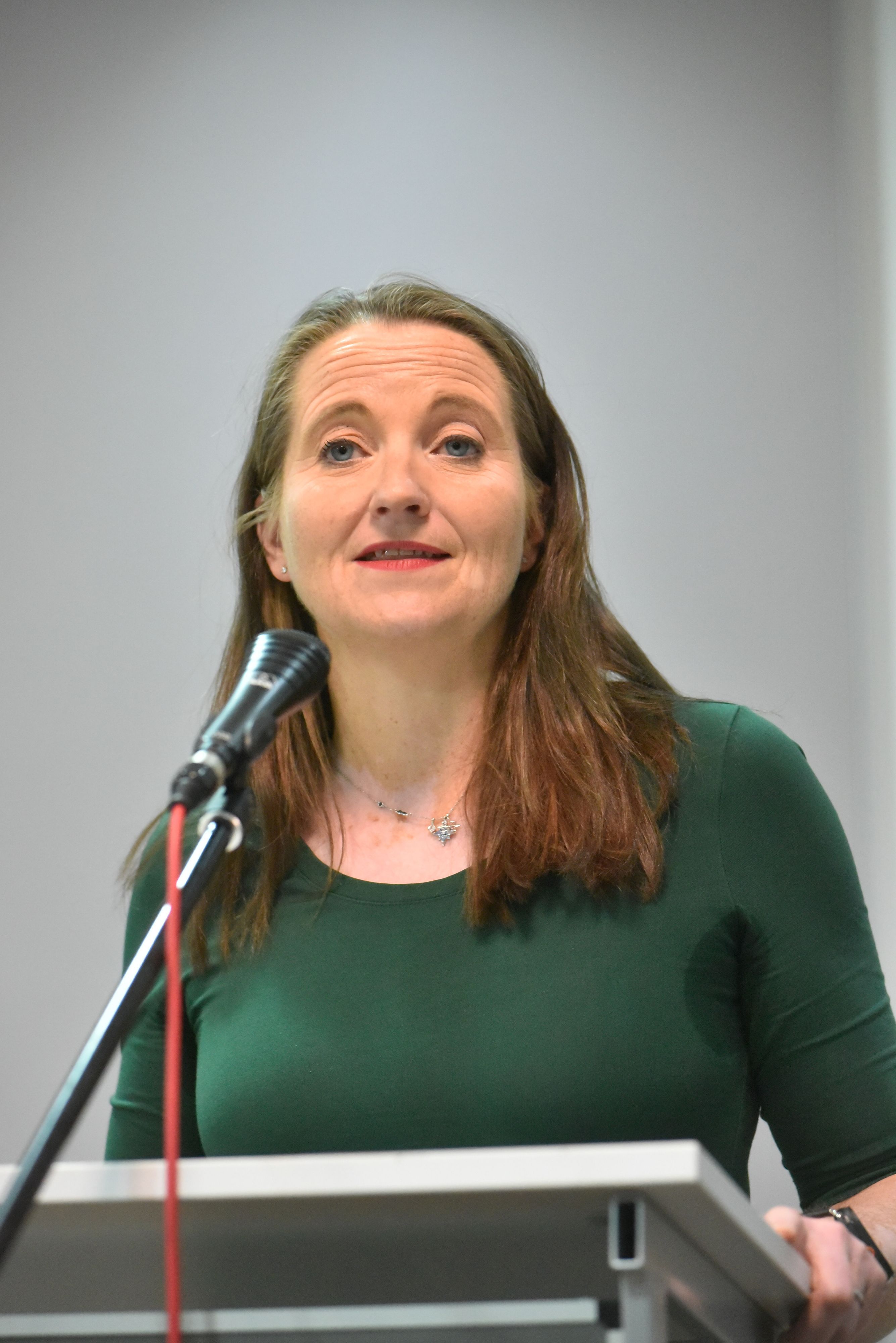 Auf dem Bild ist das Portrait einer Frau zu sehen, sie trägt ein grünes T-Shirt.