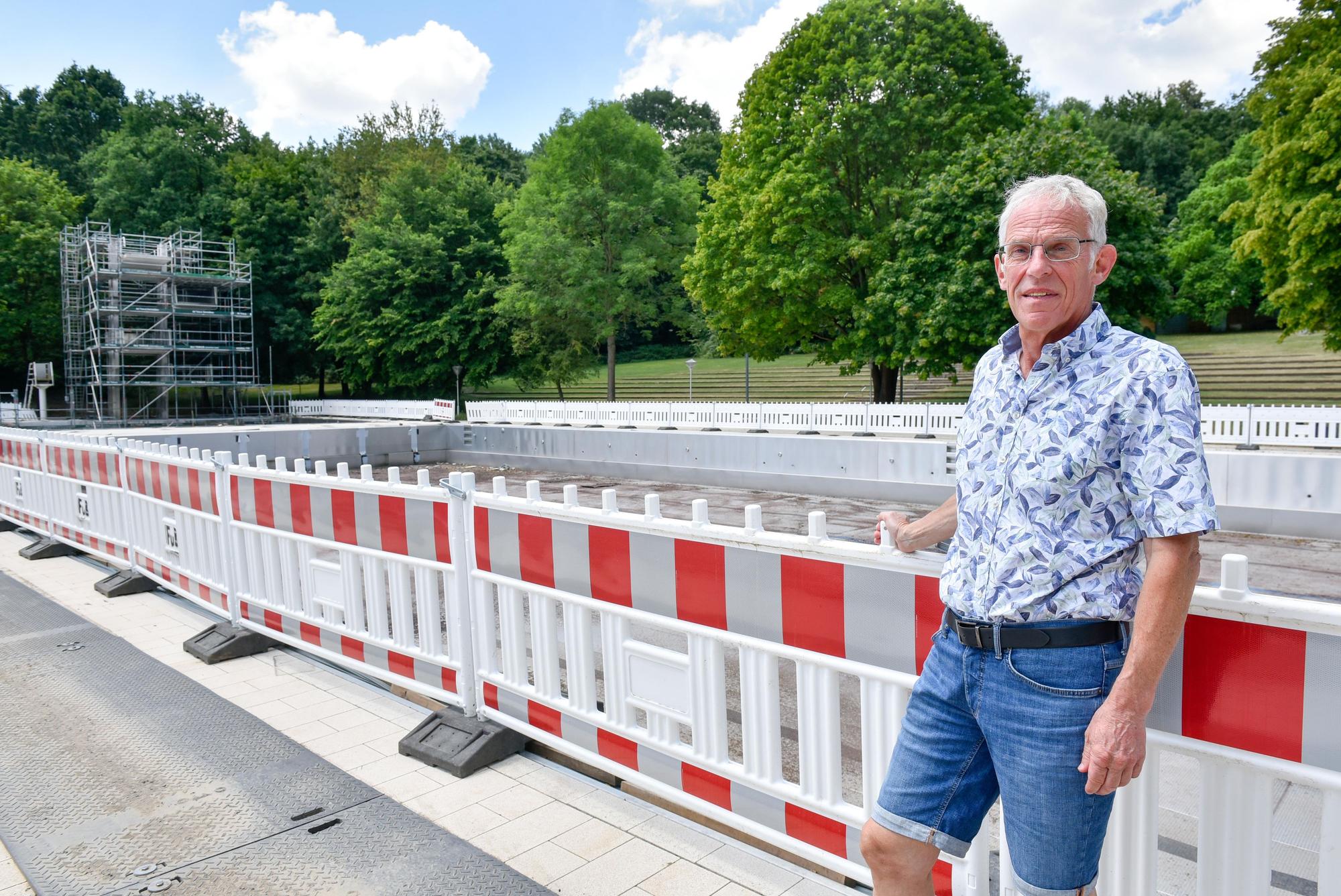 Auf dem Bild ist die Baustelle des Terassenfreibades mit Johannes Paul an einem Bauzaun zu sehen.