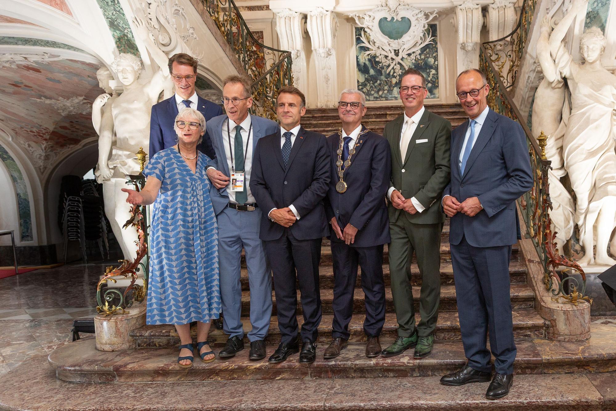 Zu sehen sind Dienstellenleiterin Regina Junga, NRW-Ministerpräsident Hendrik Wüst, Detlef Seif, Emmanuel Macron, Dr. Marc Prokop, Gregor Golland und Friedrich Merz