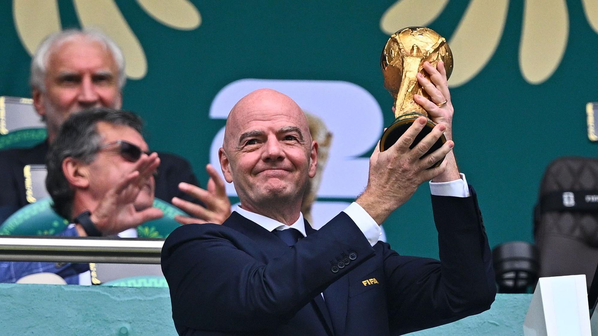 Gianni Infantino hält auf der Tribübne einen Pokal hoch.