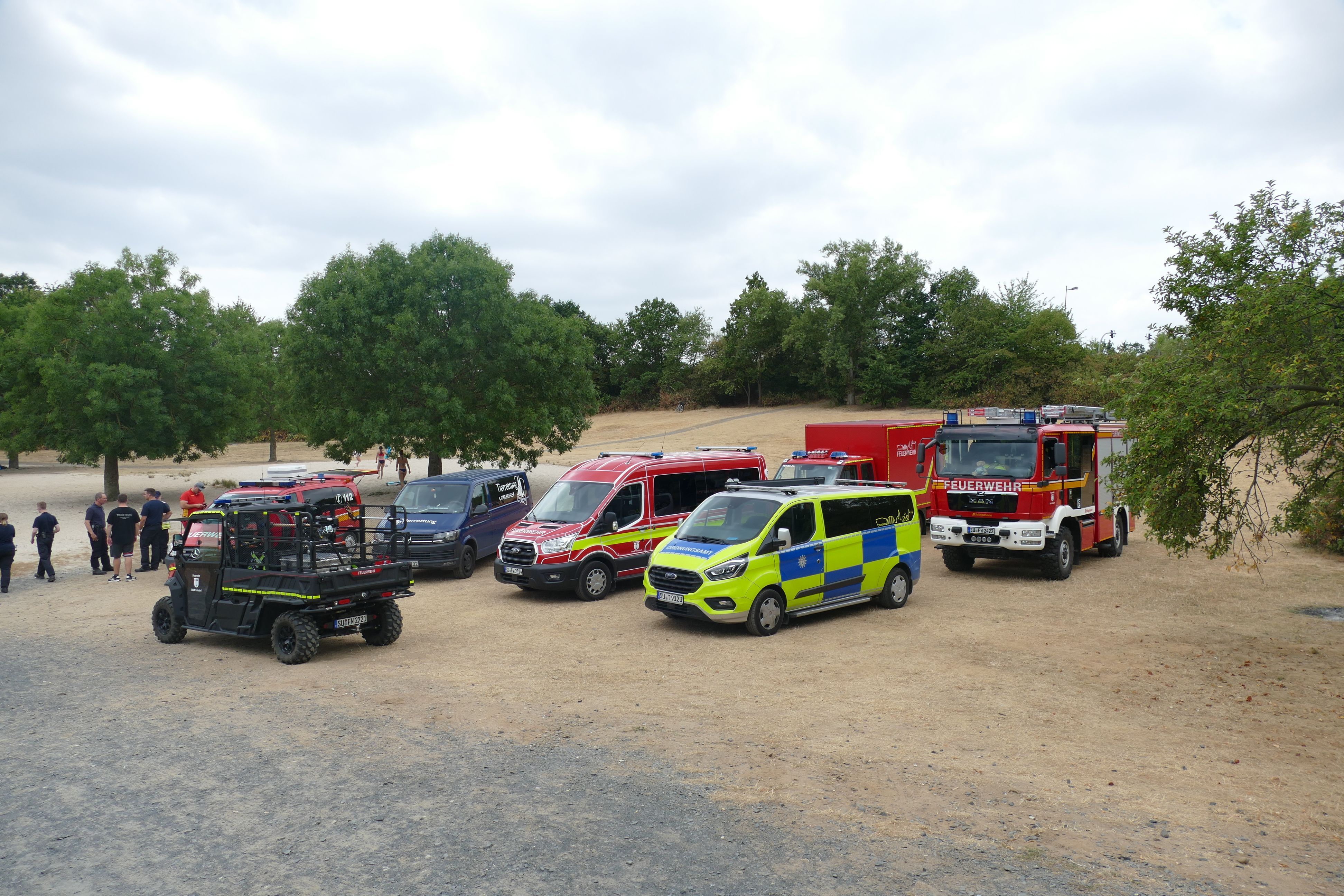 Fahrzeuge von Feuerwehr, Ordnungsamt und DLRG am Ufer eines Baggersees.