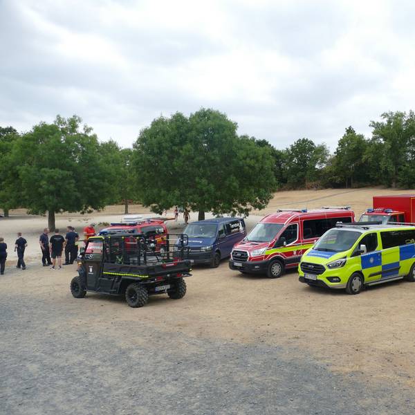 Fahrzeuge von Feuerwehr, Ordnungsamt und DLRG am Ufer eines Baggersees.
