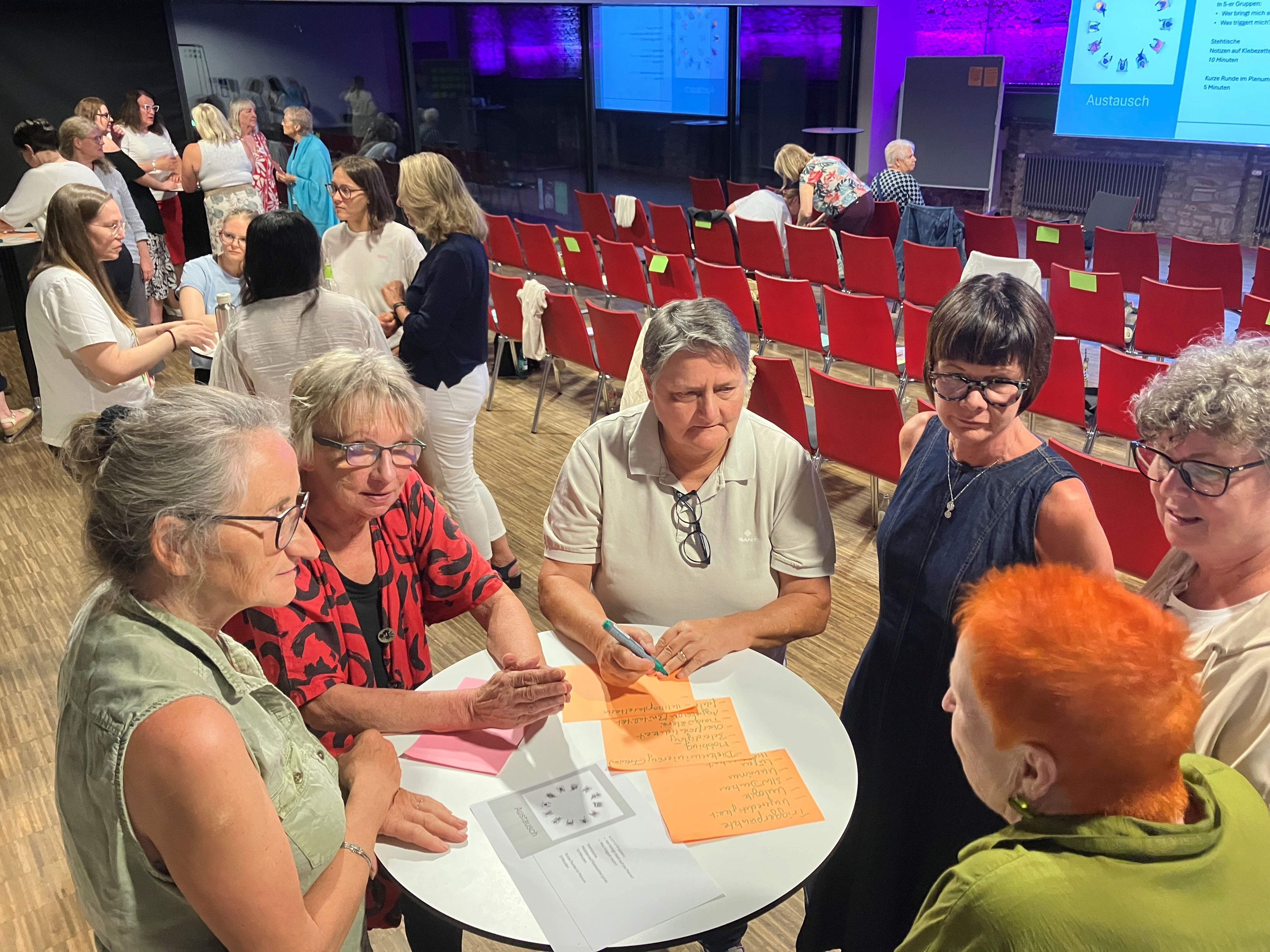 In einer Arbeitsgruppe tauschen sich sechs Teilnehmerinnen eines Workshop an einem Stehtisch untereinander aus.