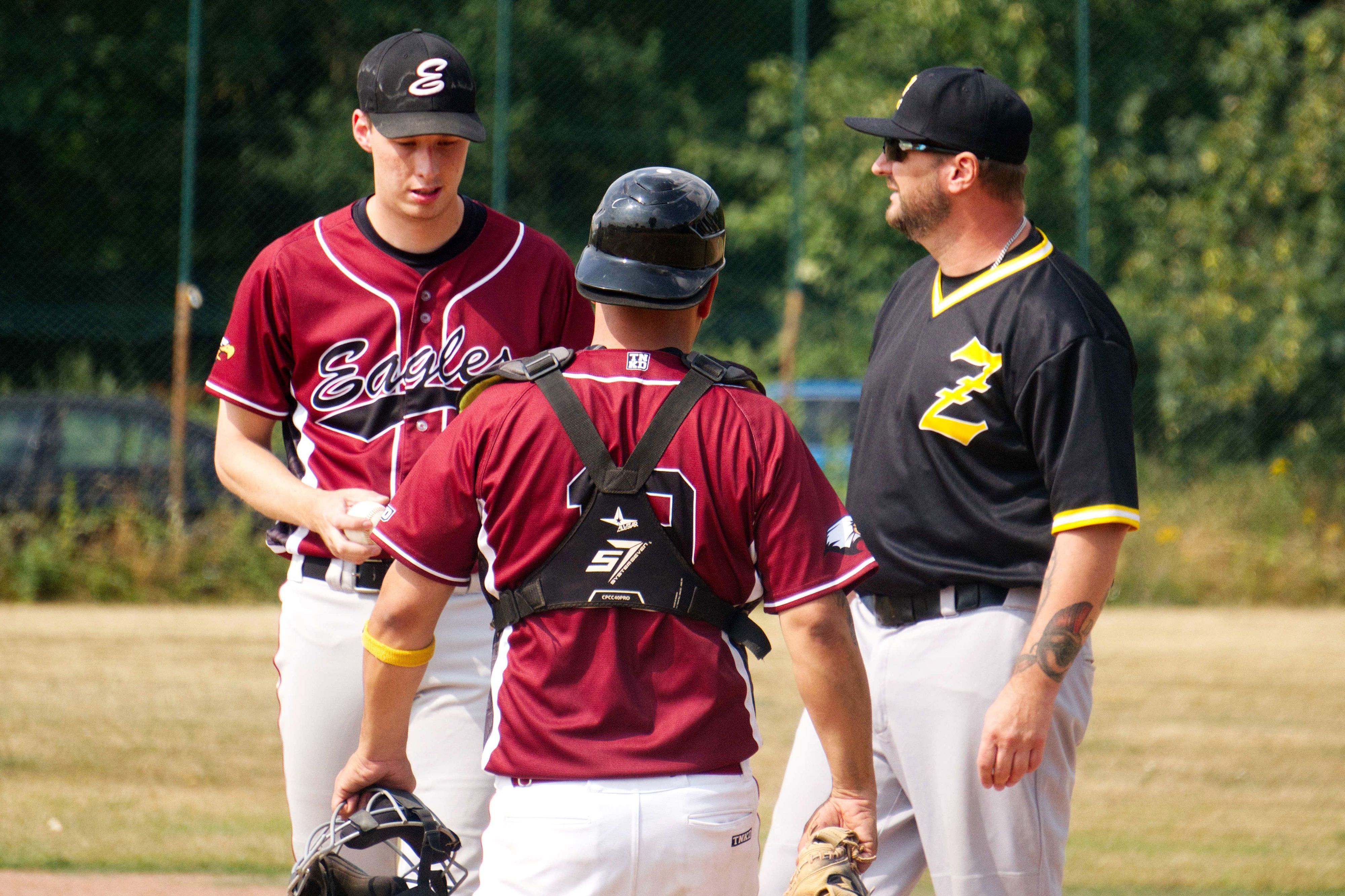 Der Trainer unterhält sich mit seinem Pitcher, der Catcher hört zu.