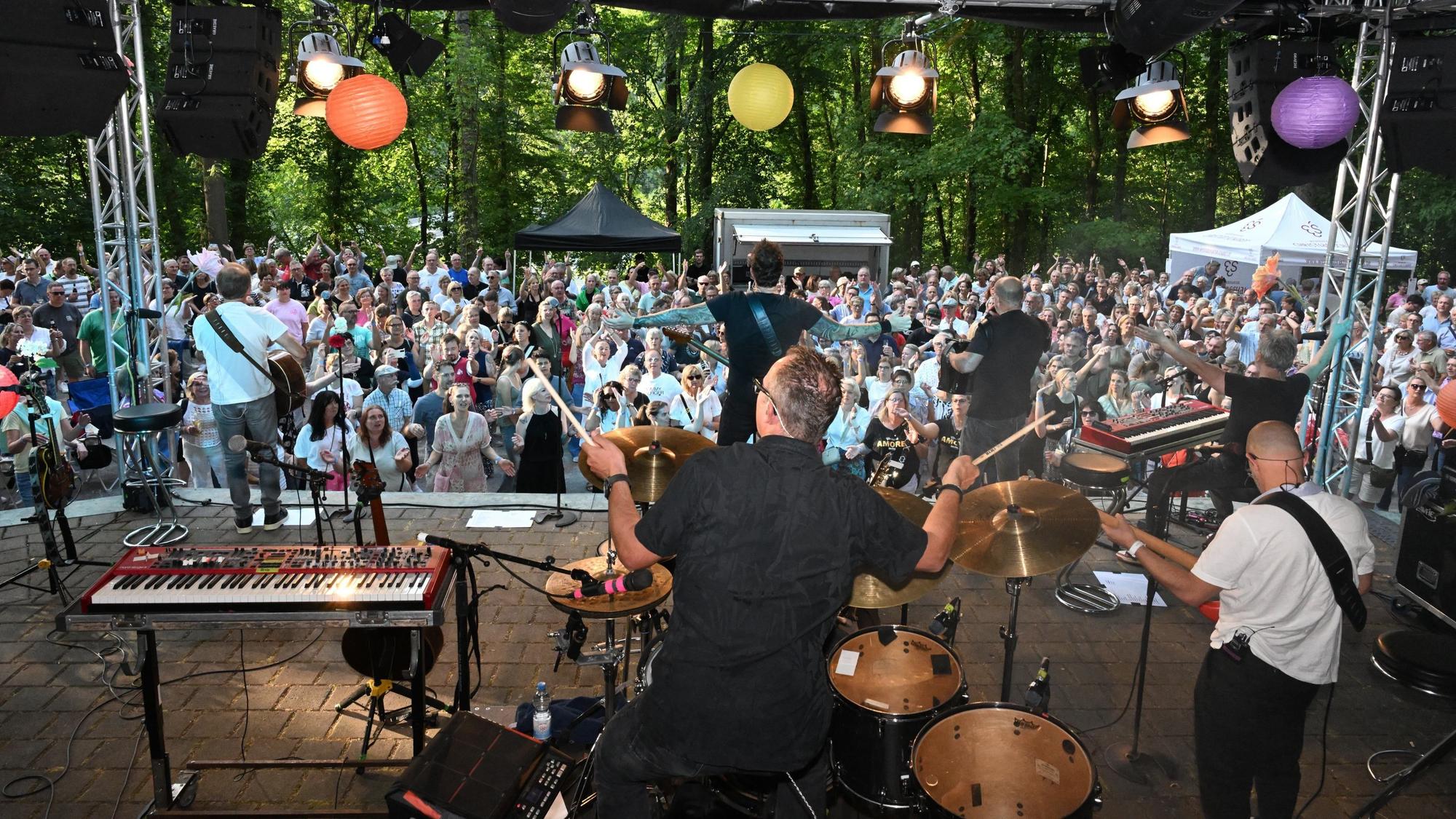 Musiker auf einer Bühne vor großem Publikum im Freien.