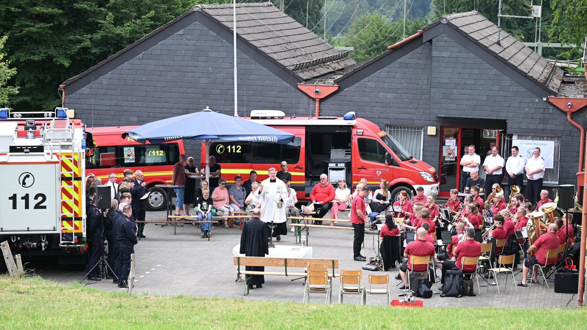 Zu sehen ist das Fest einer Feuerwehreinheit mit einem Pfarrer, der gerade spricht.