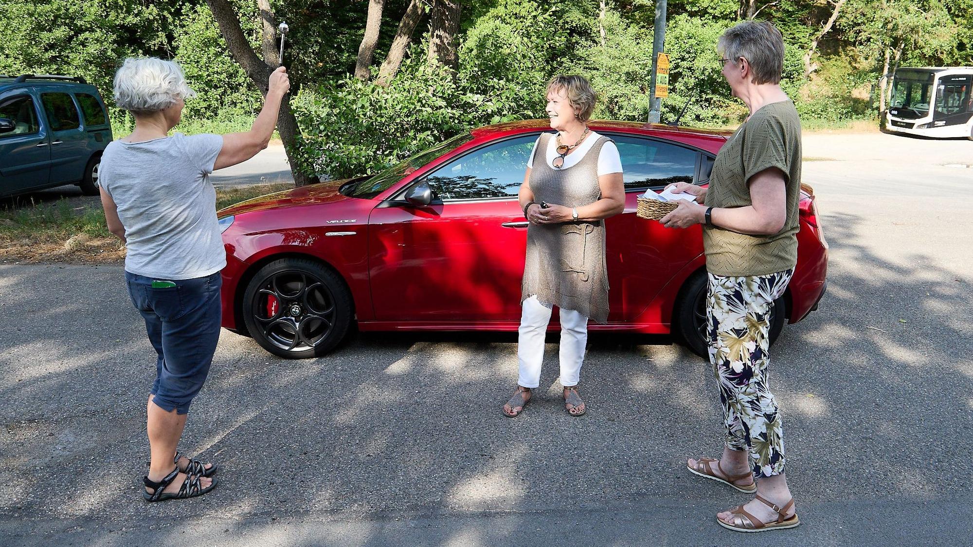 Pfarrerin Susanne Salentin spendet den Segen für zwei Frauen, im Hintergrund steht ein rotes Auto.