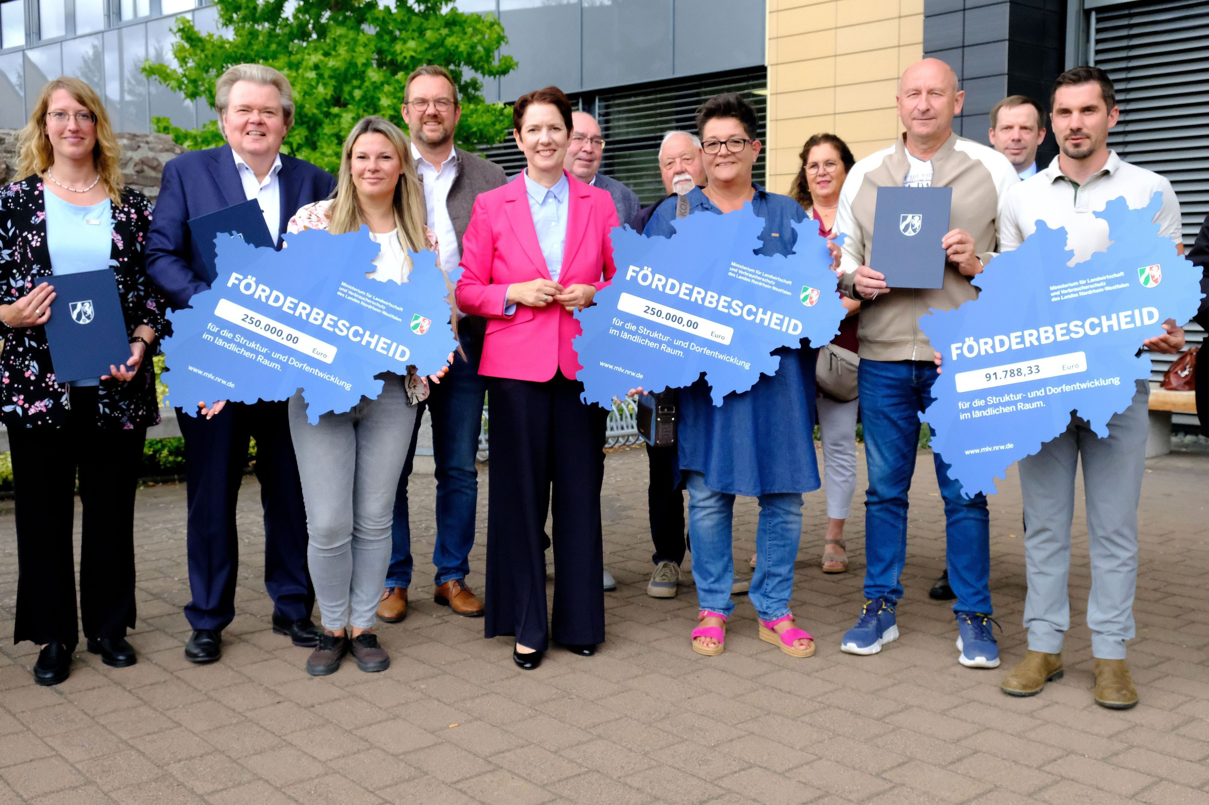 NRW-Landwirtschaftsministerin Silke Gorißen (M.) steht inmitten einer Gruppe von Männern und Frauen. Drei von ihnen halten einen Förderbescheid in den Umrissen des Landes NRW in den Händen.