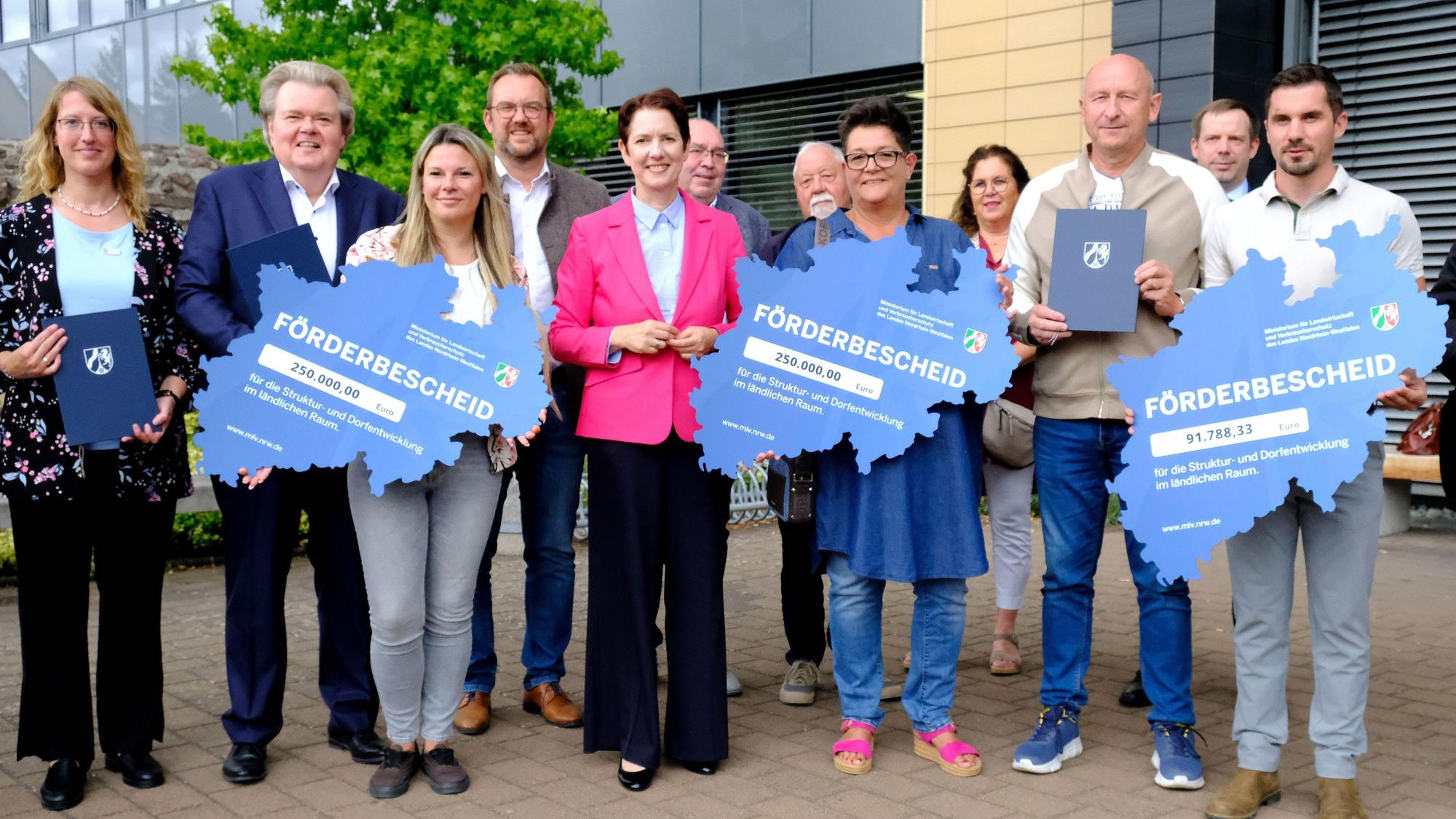 NRW-Landwirtschaftsministerin Silke Gorißen (M.) steht inmitten einer Gruppe von Männern und Frauen. Drei von ihnen halten einen Förderbescheid in den Umrissen des Landes NRW in den Händen.
