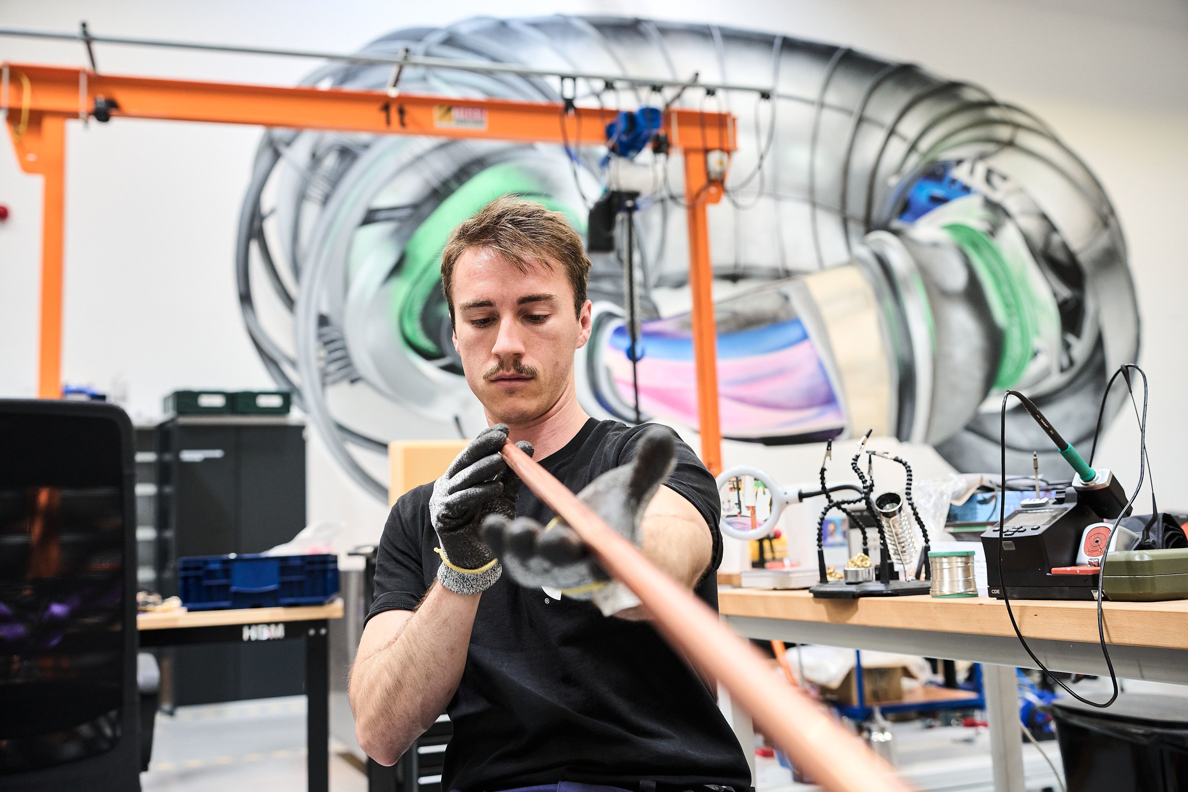 Ein Mitarbeiter von Proxima Fusion in einer Werkstatt des Start-ups. Im Hintergrund ein Modell eines Einschlussmagneten.