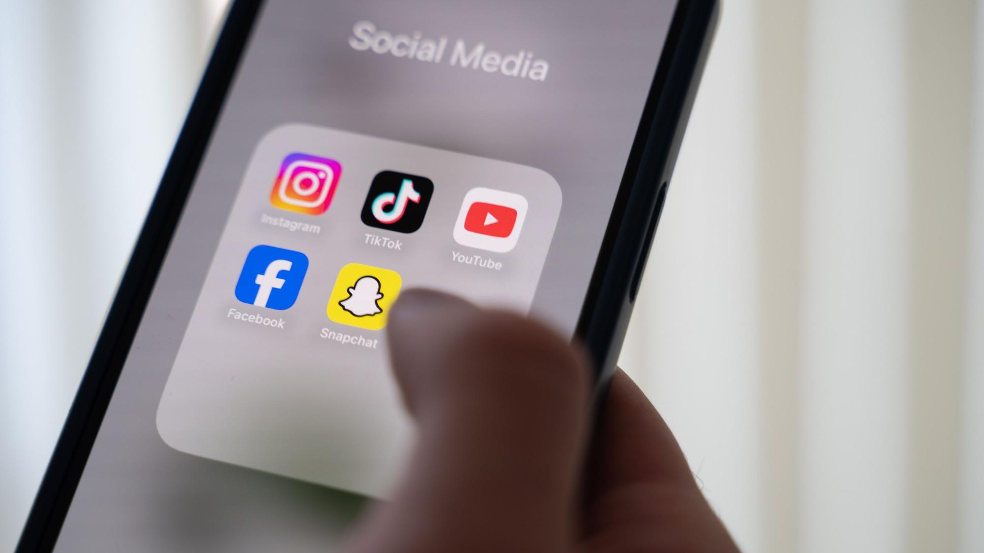 Eine Frau hält ein Smartphone, auf dessen Display verschiedene Social Media Apps angezeigt werden.