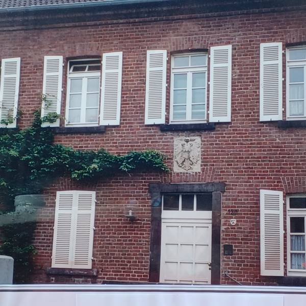 Die Fenster eines zweigeschossigen Backsteingebäudes haben weiße Fensterläden.