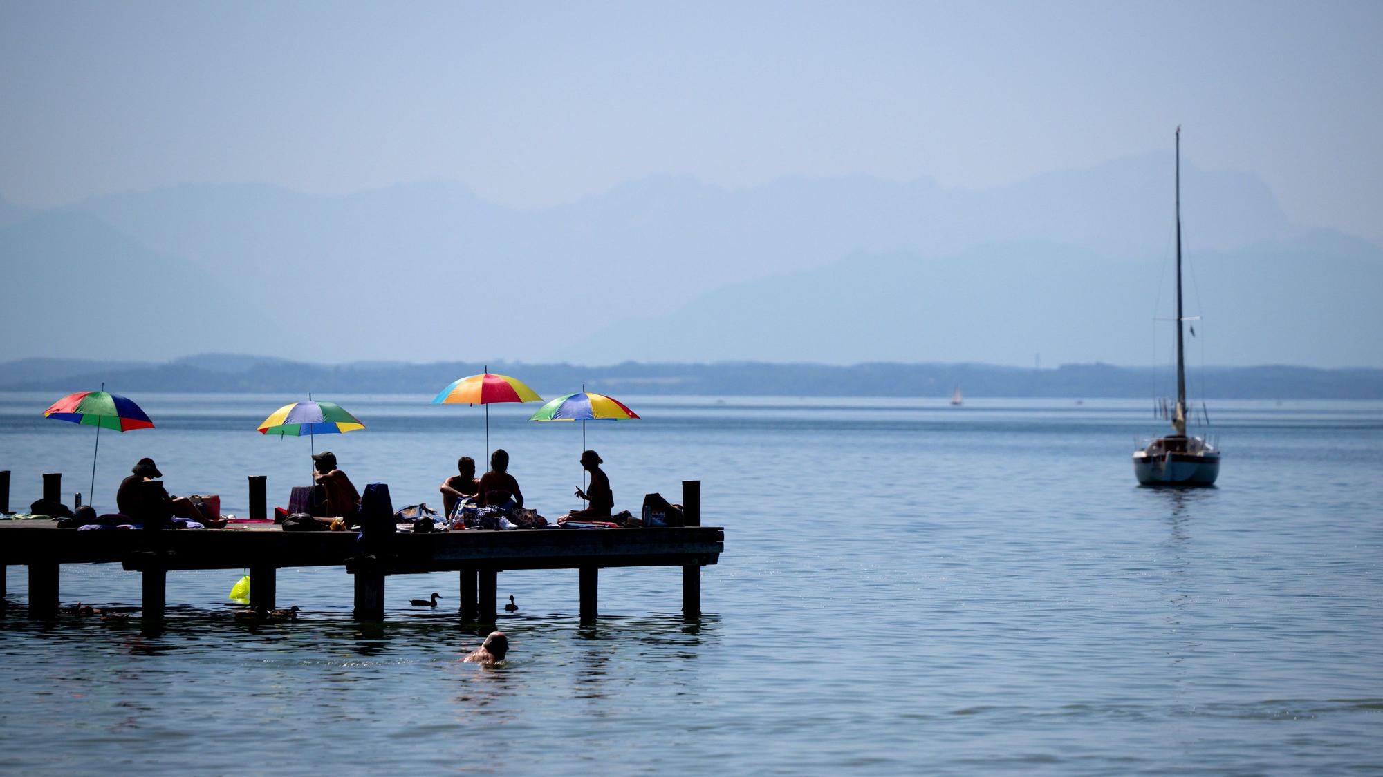 AMenschen genießen das warme Wetter und den Sonnenschein auf einem Steg am Starnberger See.