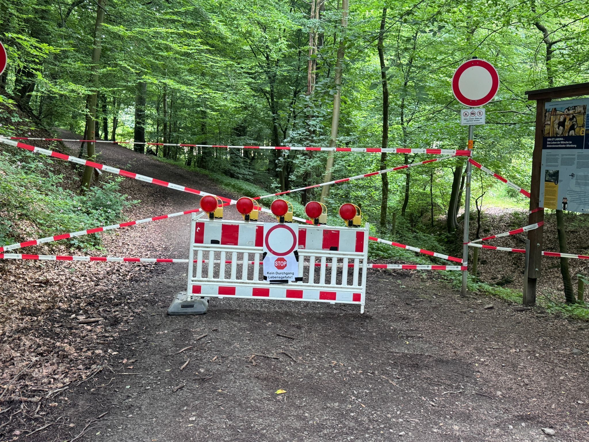 Eine weiß-rote Absperrbake vor einem Wanderweg. Darauf ein Schild mit der Warnung: "Kein Durchgang. Lebensgefahr!"