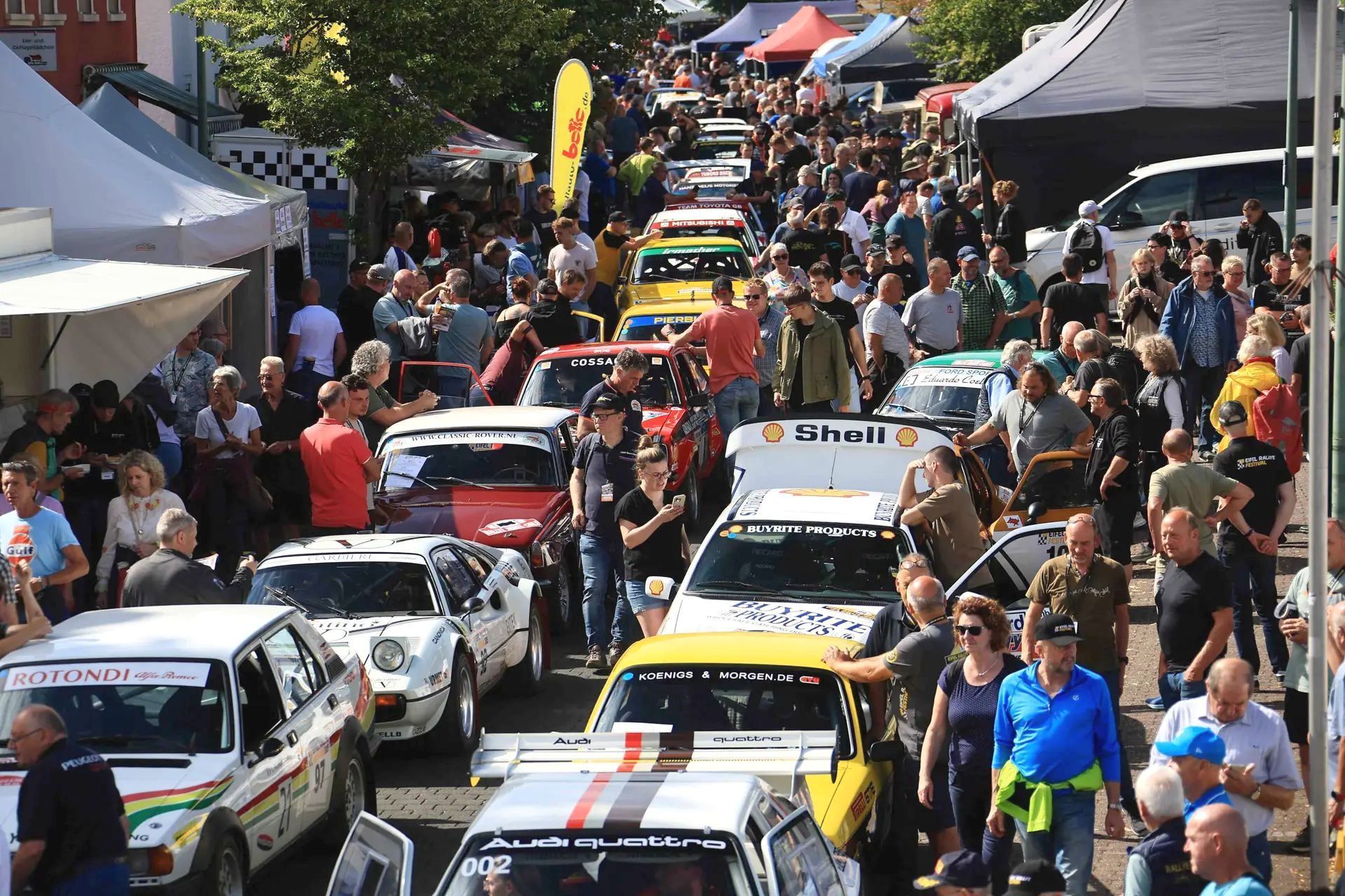 Bei der Rallye-Meile in der Dauner Innenstadt schlängeln sich zahlreiche Menschen durch die in Doppelreihe parkenden historischen Rennwagen.