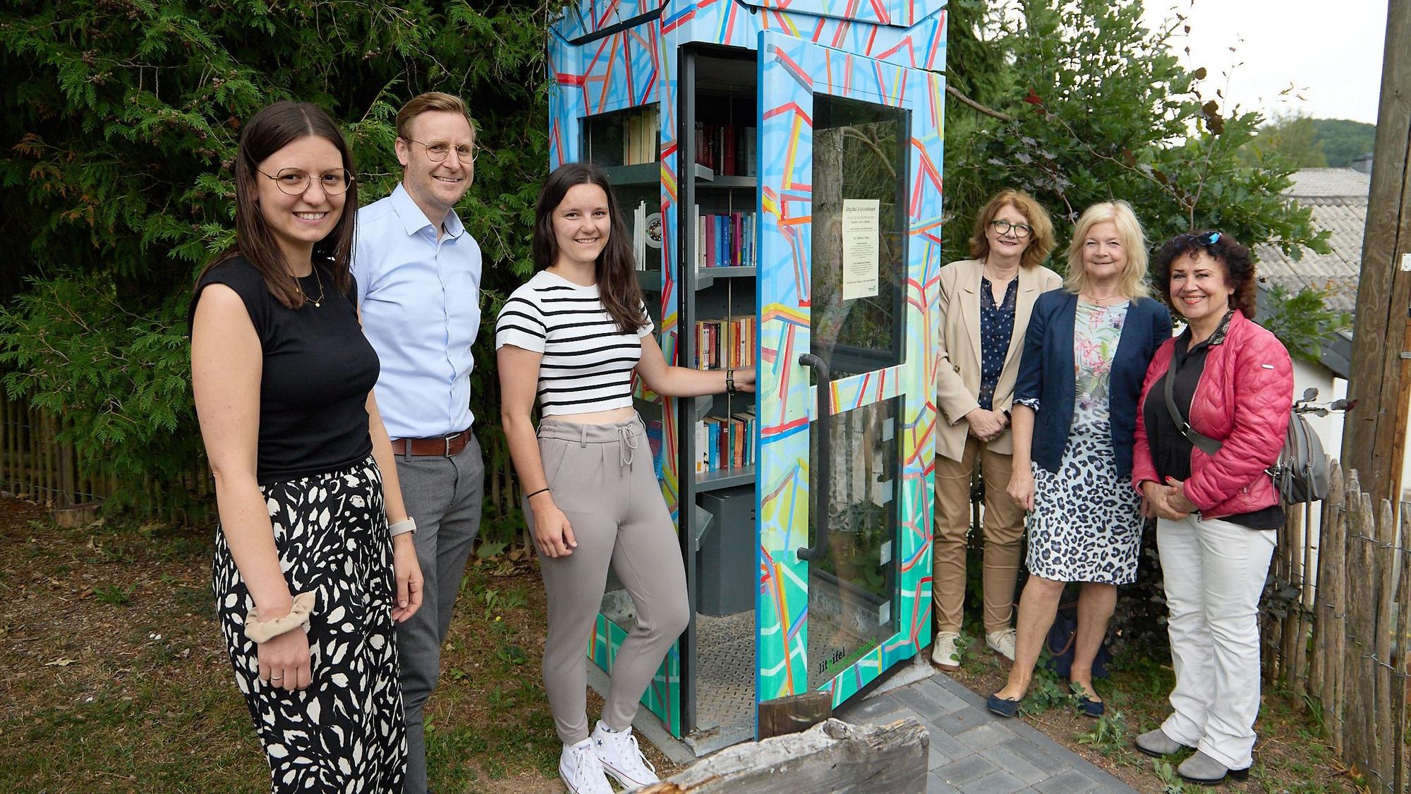Fünf Frauen und ein Mann stehen rechts und links neben einer alten Telefonzelle. Die ist bunt bemalt und wird nun als Bücherschrank genutzt.