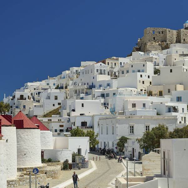 Blick auf die weiß getünchte Siedlung Chora mit den Windmühlen und der Burg Querini auf der griechischen Insel Astypalea unter strahlend blauem Himmel.