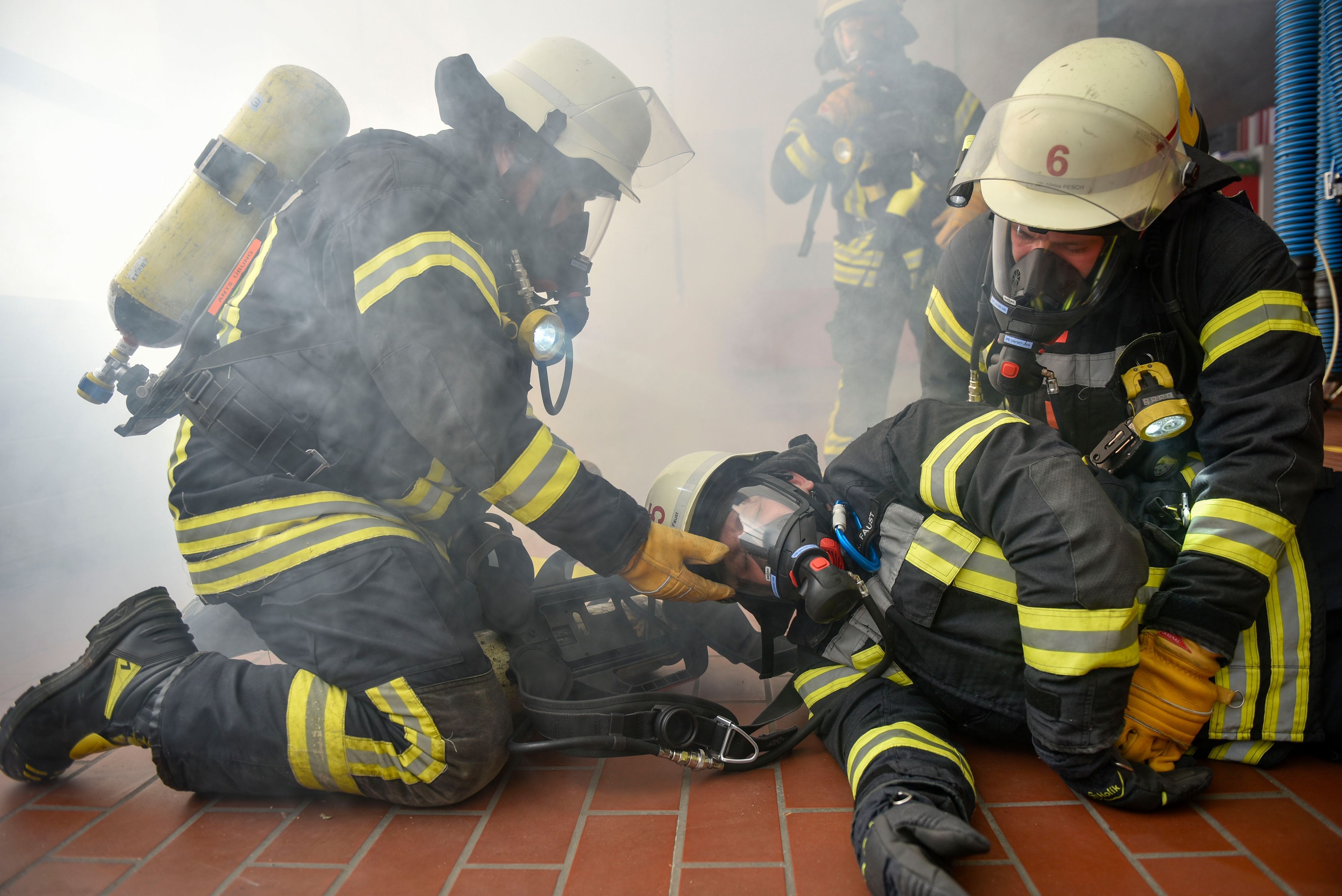 Das Bild zeigt Feuerwehrmänner mit Atemschutzmasken, die einen Kollegen retten.