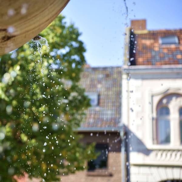 Aus einem Brunnen tropft Wasser, im Hintergrund sind Häuser und Bäume zu erkennen.