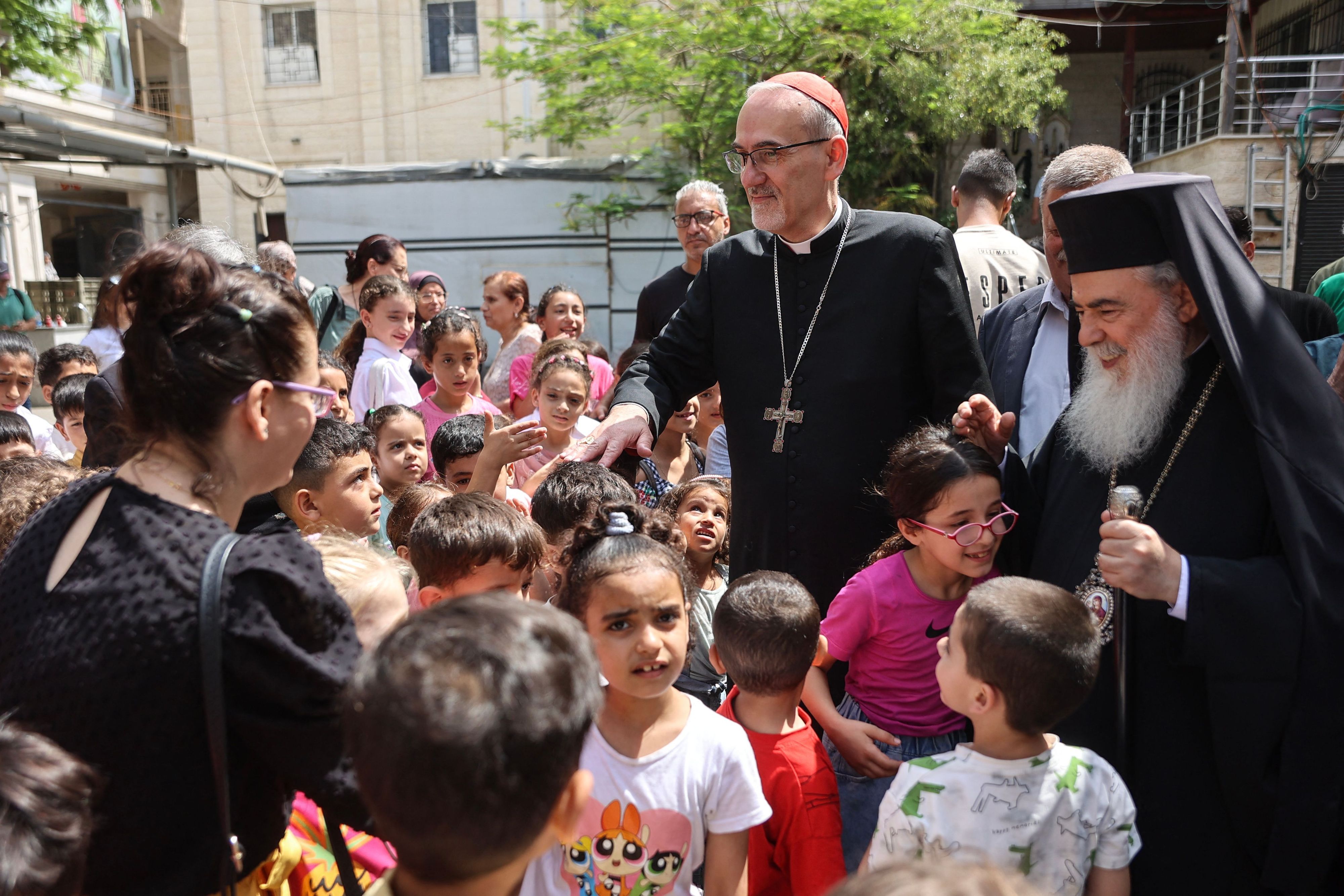 Jerusalem's Latin Patriarch Cardinal Pierbattista Pizzaballa (2nd R) and Greek Orthodox Patriarch of Jerusalem Theophilos III (R) meet with children during a visit to the Holy Family Church in Gaza City on June 22, 2026. Pizzaballa pledged on June 22 not to abandon Gaza's Christian community as he visited the territory with his Greek Orthodox counterpart. Pizzaballa and Patriarch Theophilos III arrived for a pastoral visit aimed at supporting both Gaza's small Christian population and its wider community after years of war and hardship. (Photo by Omar AL-QATTAA / AFP)