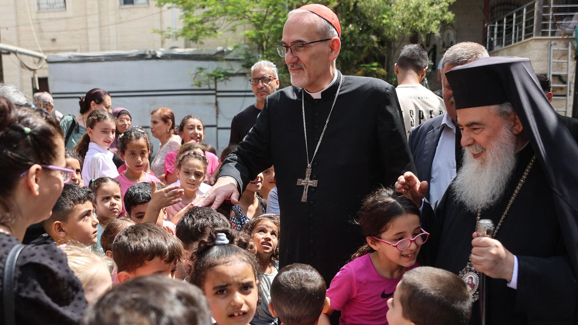 Jerusalem's Latin Patriarch Cardinal Pierbattista Pizzaballa (2nd R) and Greek Orthodox Patriarch of Jerusalem Theophilos III (R) meet with children during a visit to the Holy Family Church in Gaza City on June 22, 2026. Pizzaballa pledged on June 22 not to abandon Gaza's Christian community as he visited the territory with his Greek Orthodox counterpart. Pizzaballa and Patriarch Theophilos III arrived for a pastoral visit aimed at supporting both Gaza's small Christian population and its wider community after years of war and hardship. (Photo by Omar AL-QATTAA / AFP)