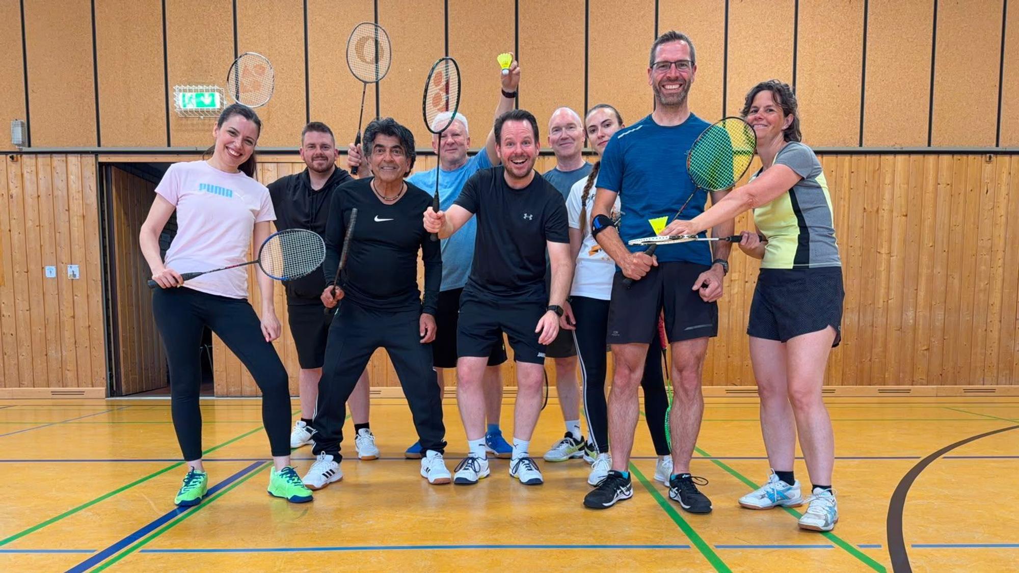 Frauen und Männer mit Badminton-Schlägern und Federbällen stehen in einer Halle.