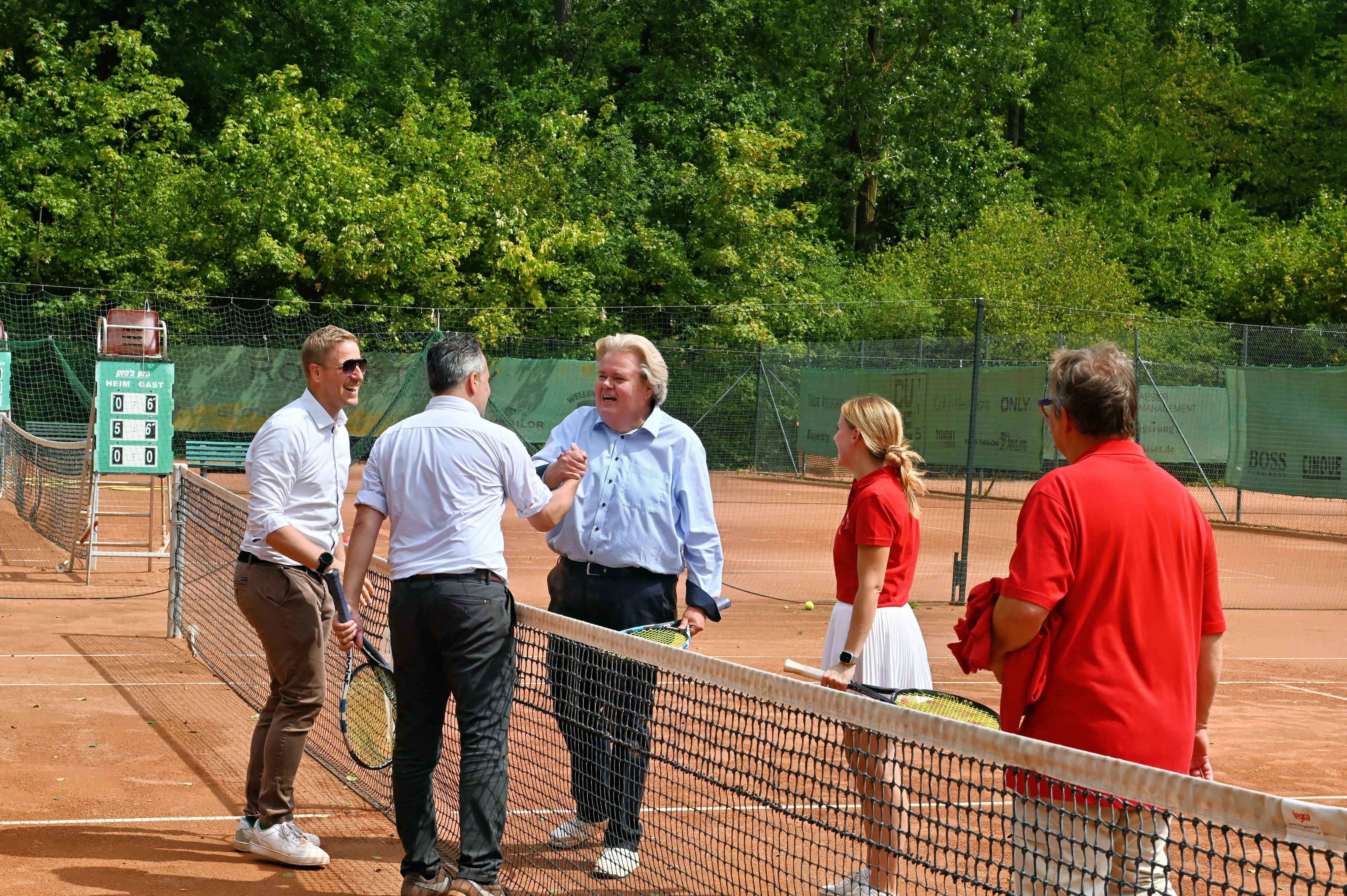 Markus Ramers, Klaus Voussem und Sacha Reichelt stehen auf dem Tennisplatz am Netz, neben ihnen zwei Vereinsmitglieder.